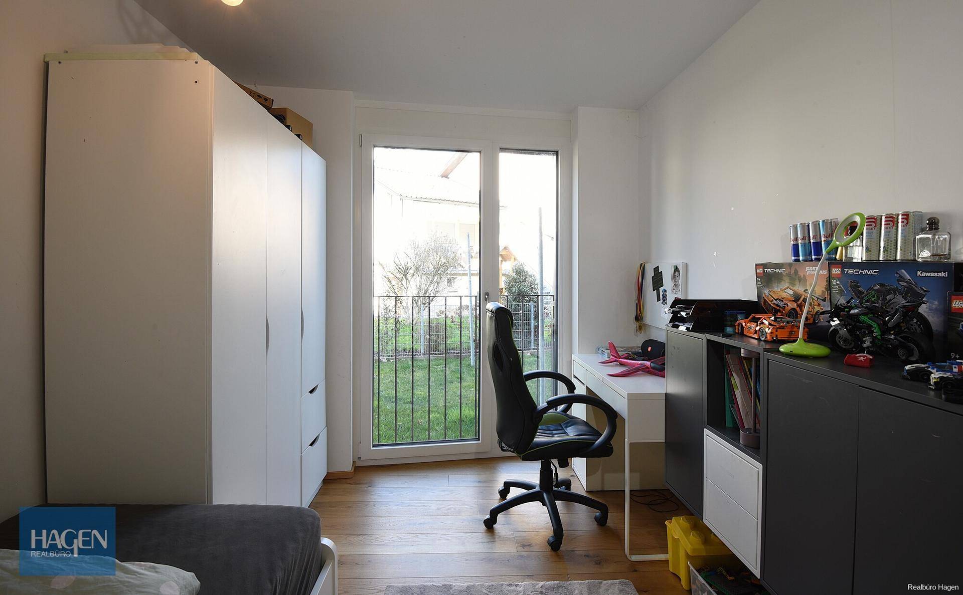 Helles Zimmer mit Schreibtisch, Kleiderschrank und Zugang zu einem französischen Balkon.