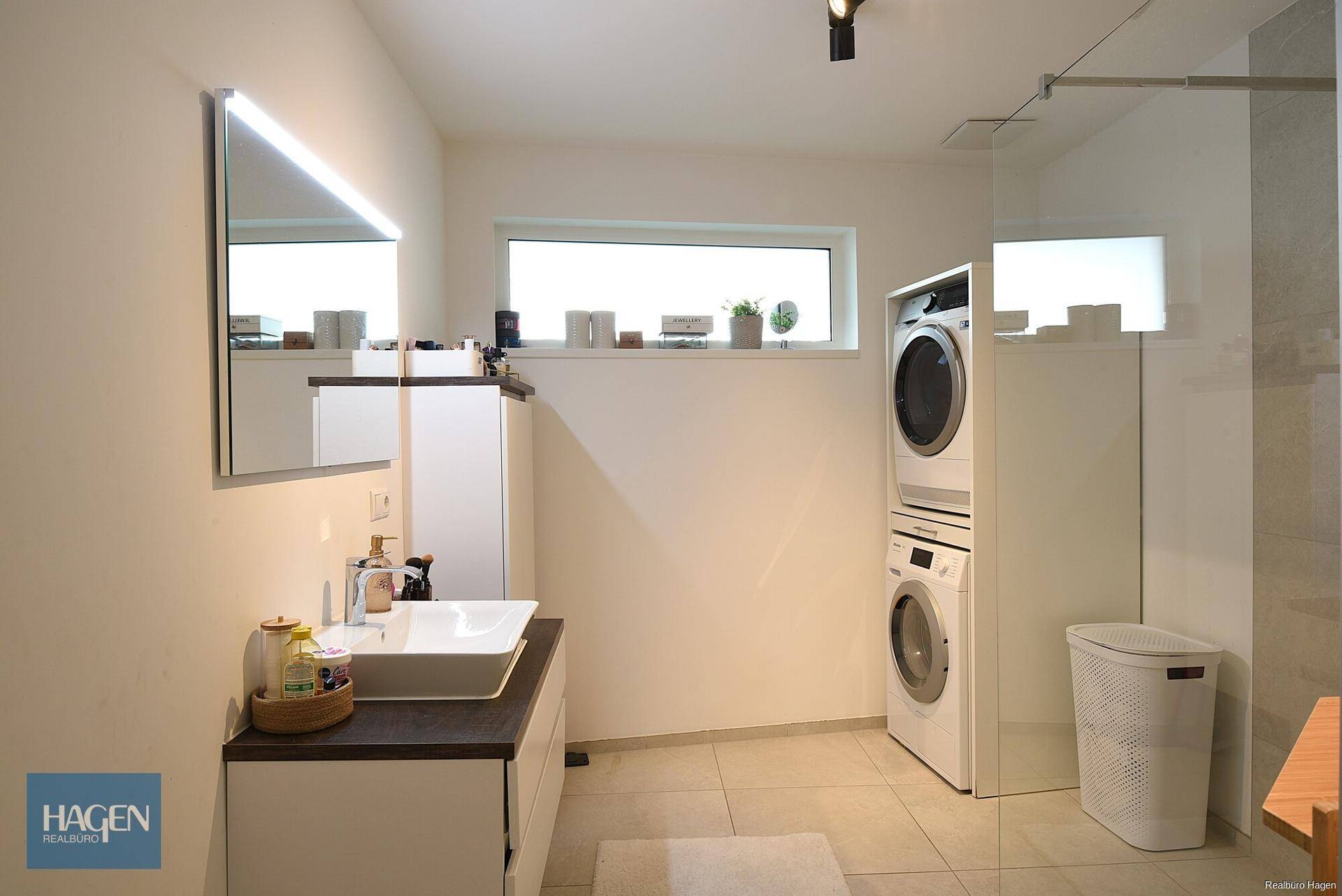 Modernes Badezimmer mit Waschmaschine, Trockner und großem Fenster für Tageslicht.