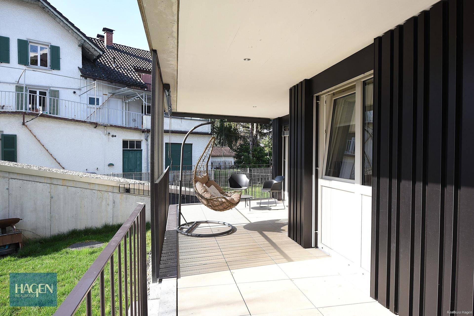 Geräumiger Balkon mit Hängesessel, Sitzgelegenheiten und Blick auf die grüne Umgebung.