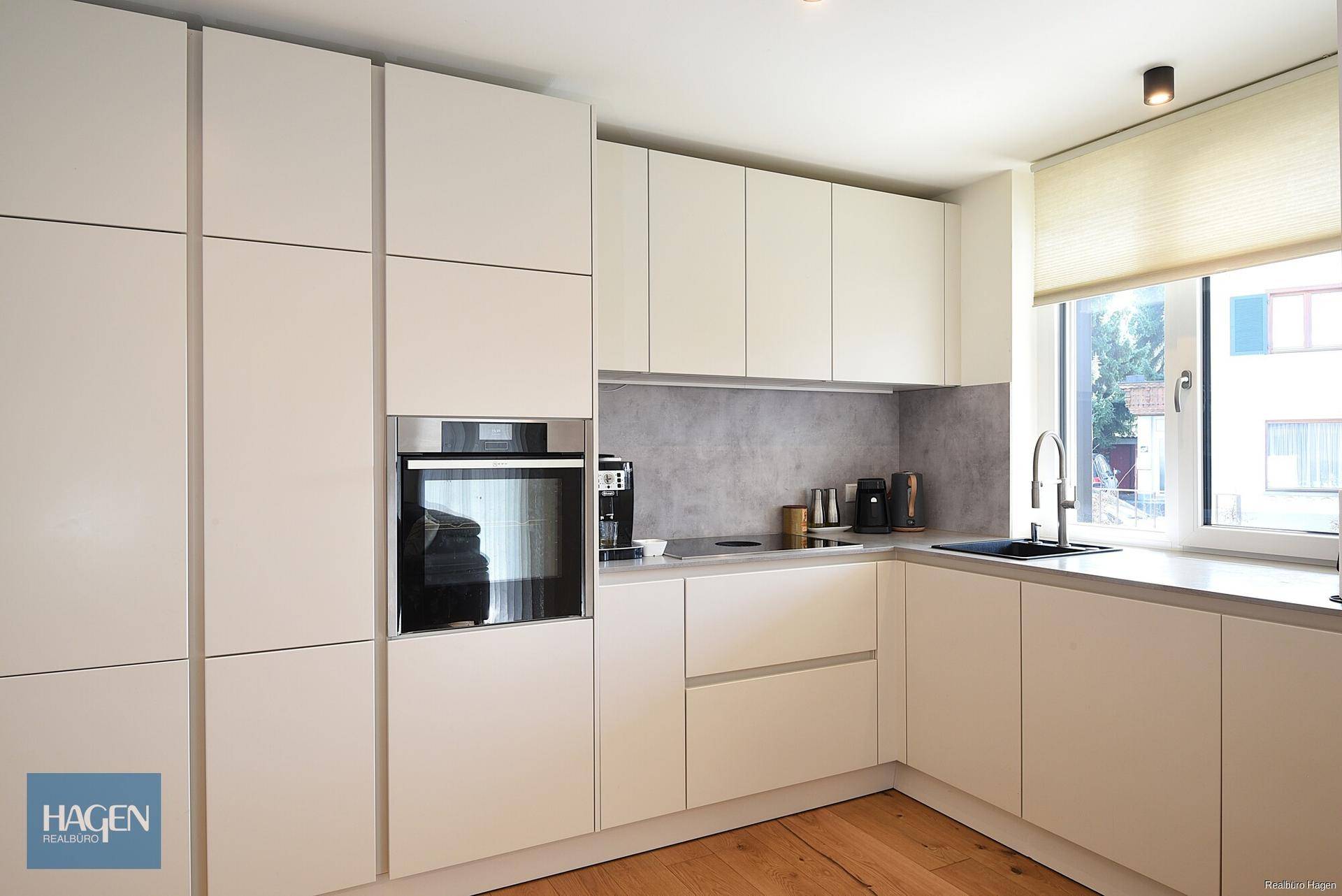 Moderne Einbauküche mit weißen Fronten, integrierten Geräten und Fenster für Tageslicht.