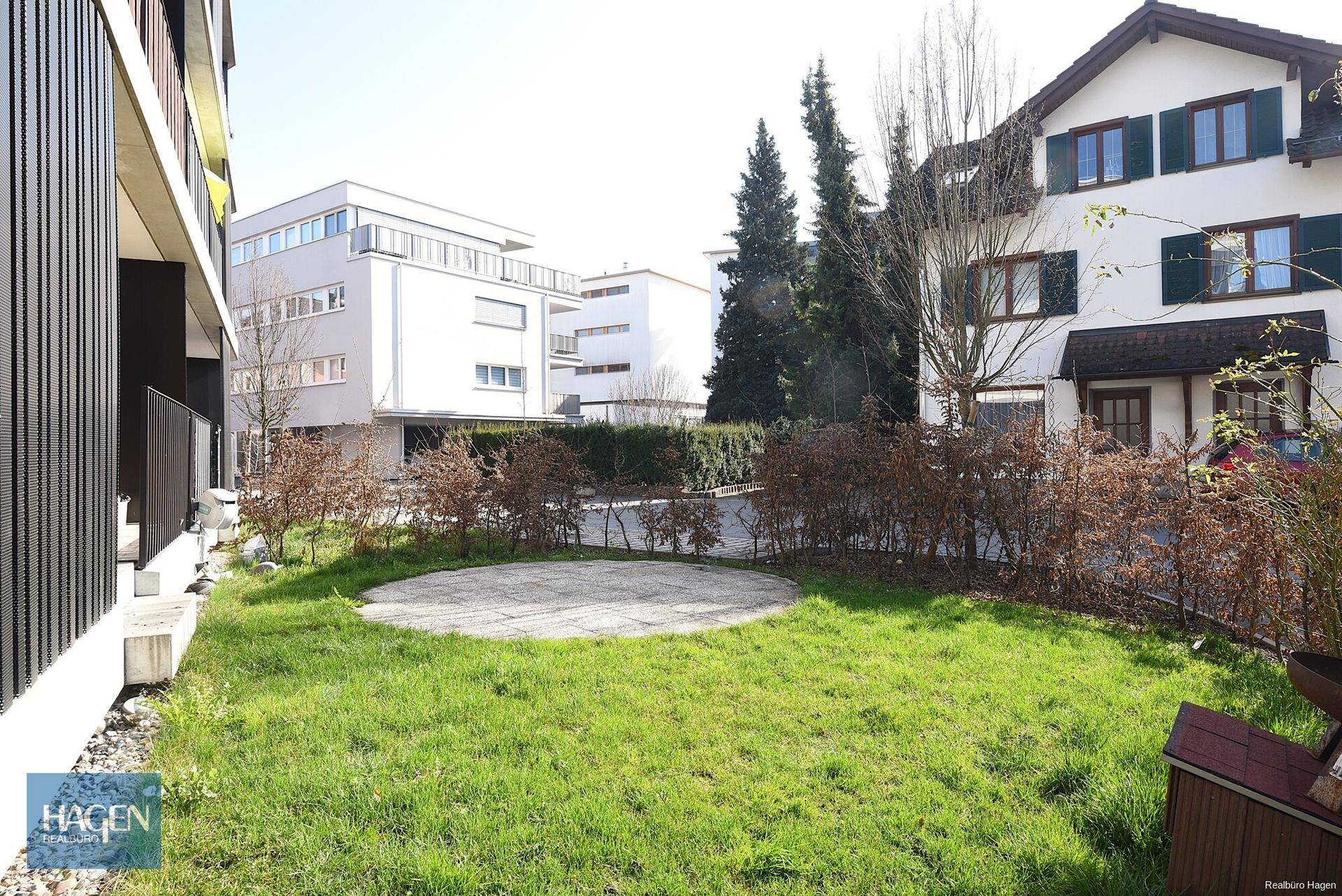 Grüner Gartenbereich mit Rasenfläche und gepflastertem Sitzplatz im Freien.
