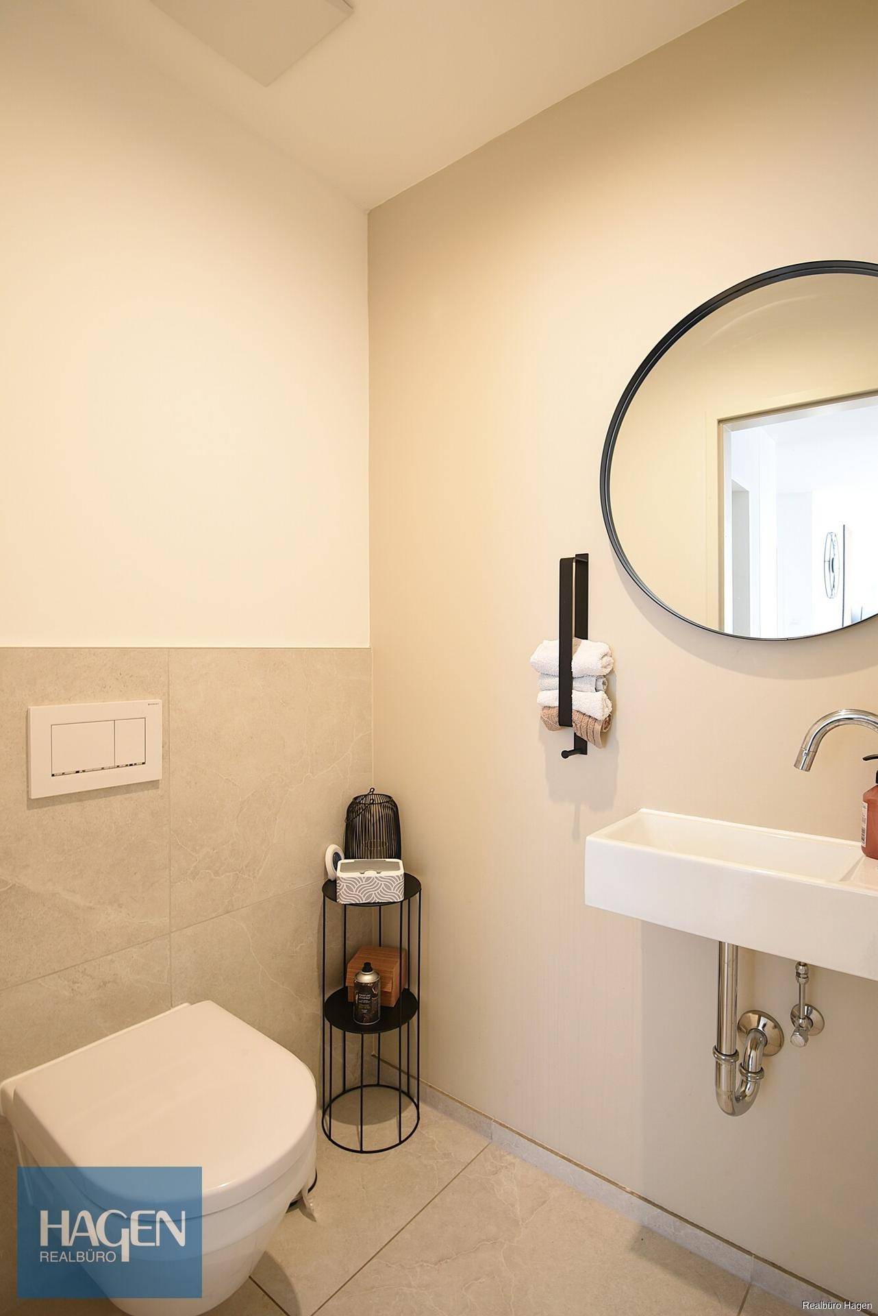 Modernes Gäste-WC mit Wand-WC, kleinem Waschbecken und rundem Spiegel.
