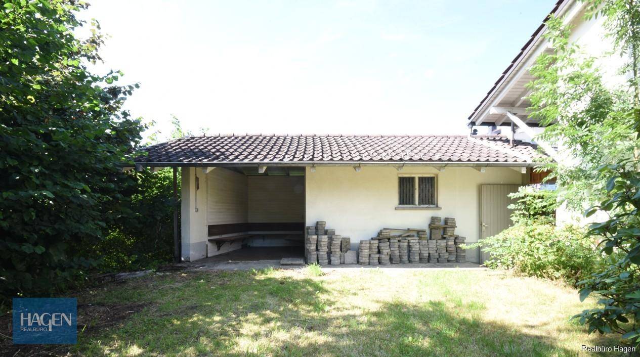 Kleines Nebengebäude mit überdachtem Bereich und gelagerten Pflastersteinen im Garten.
