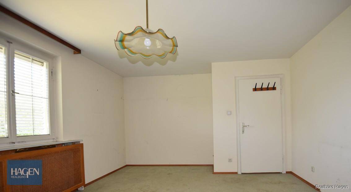 Helles Zimmer mit Teppichboden, Fenster und einer auffälligen Deckenleuchte.