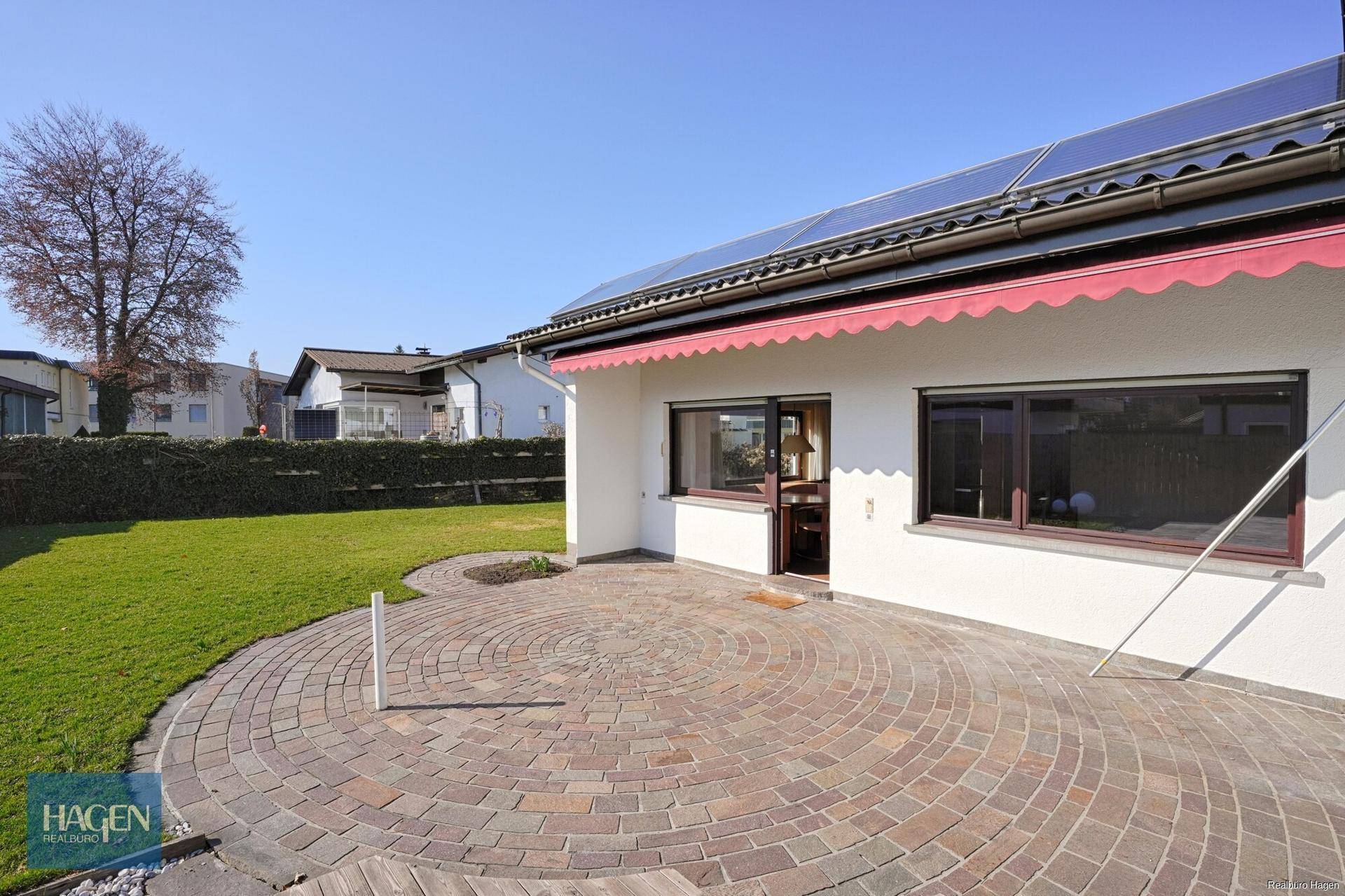Gemütliche gepflasterte Terrasse am Haus mit Markise und Gartenblick.