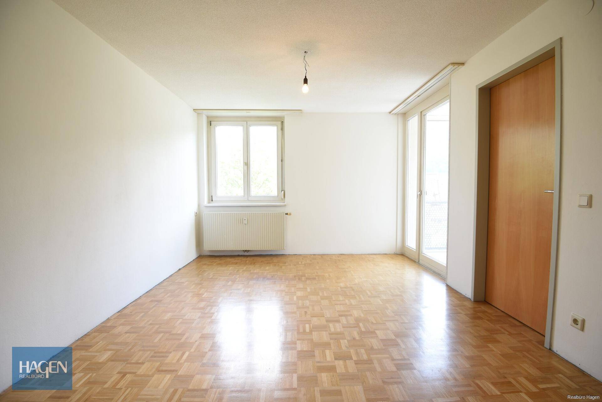 Heller, leerer Raum mit Parkettboden, weißen Wänden und Zugang zu einem Balkon oder einer Terrasse.