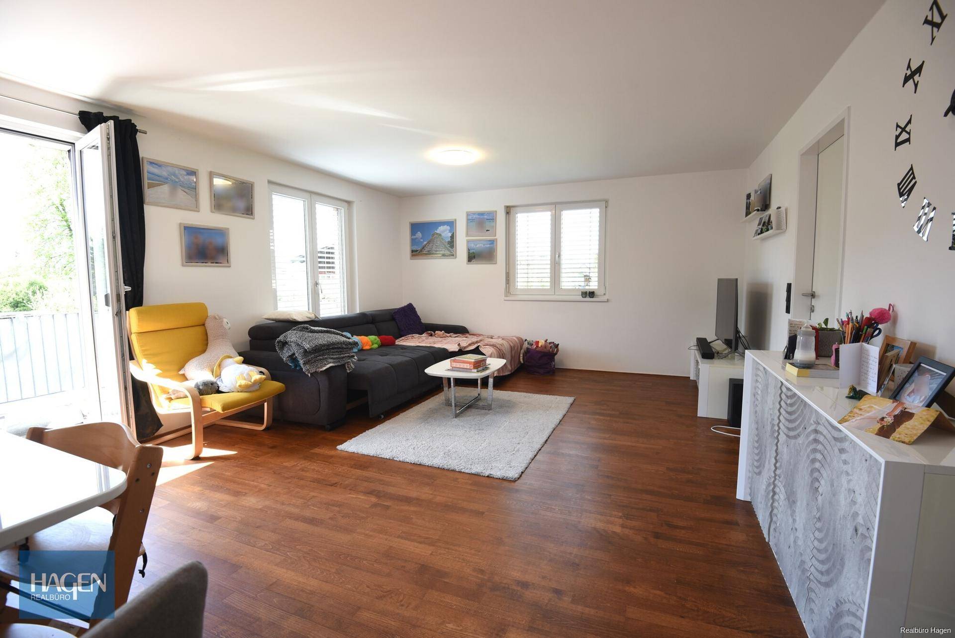 Geräumiges Wohnzimmer mit bequemer Couch, Holzboden und großen Fenstern mit Balkonzugang.