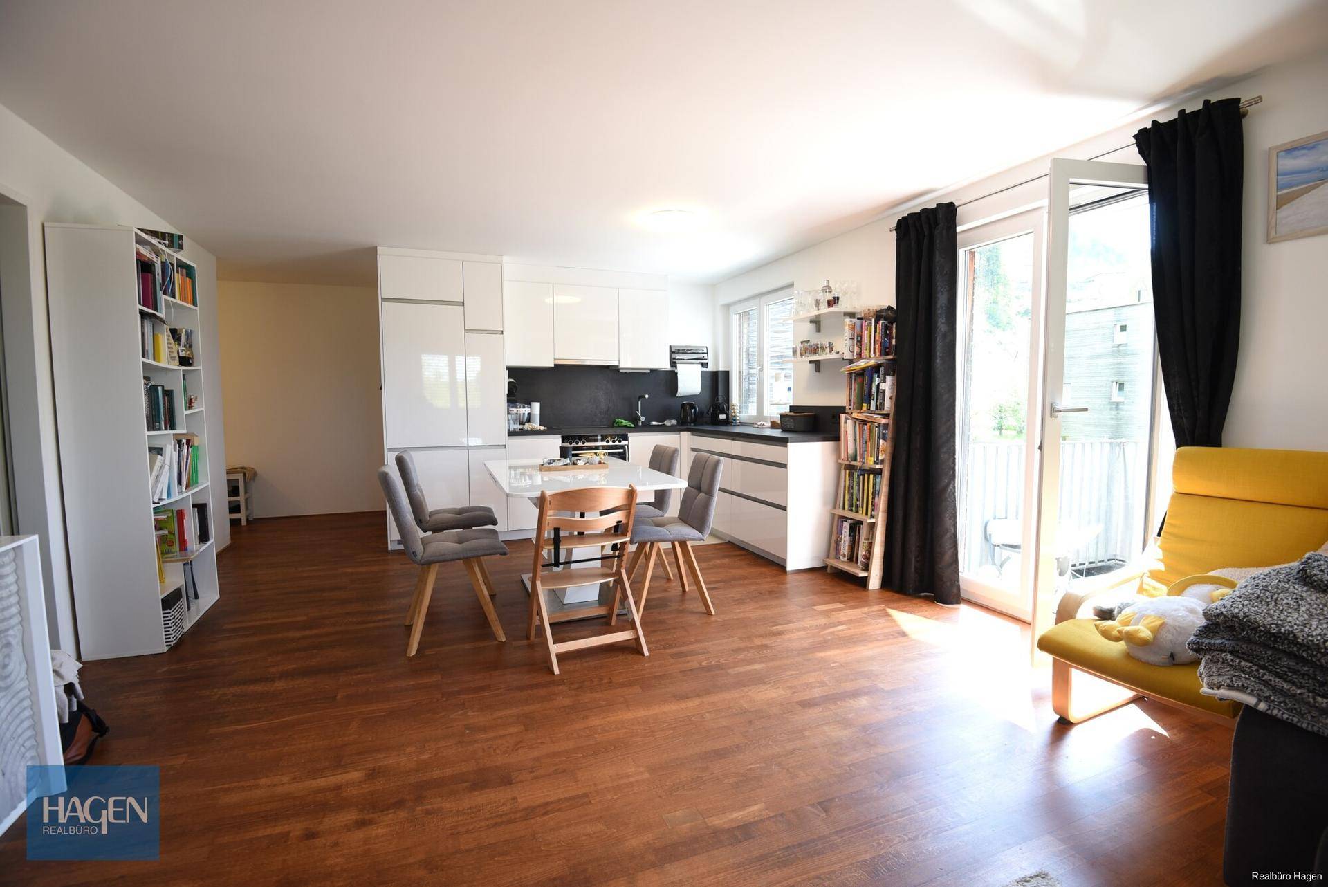 Heller offener Wohn- und Essbereich mit moderner Küche, Holzboden und Zugang zum Balkon.