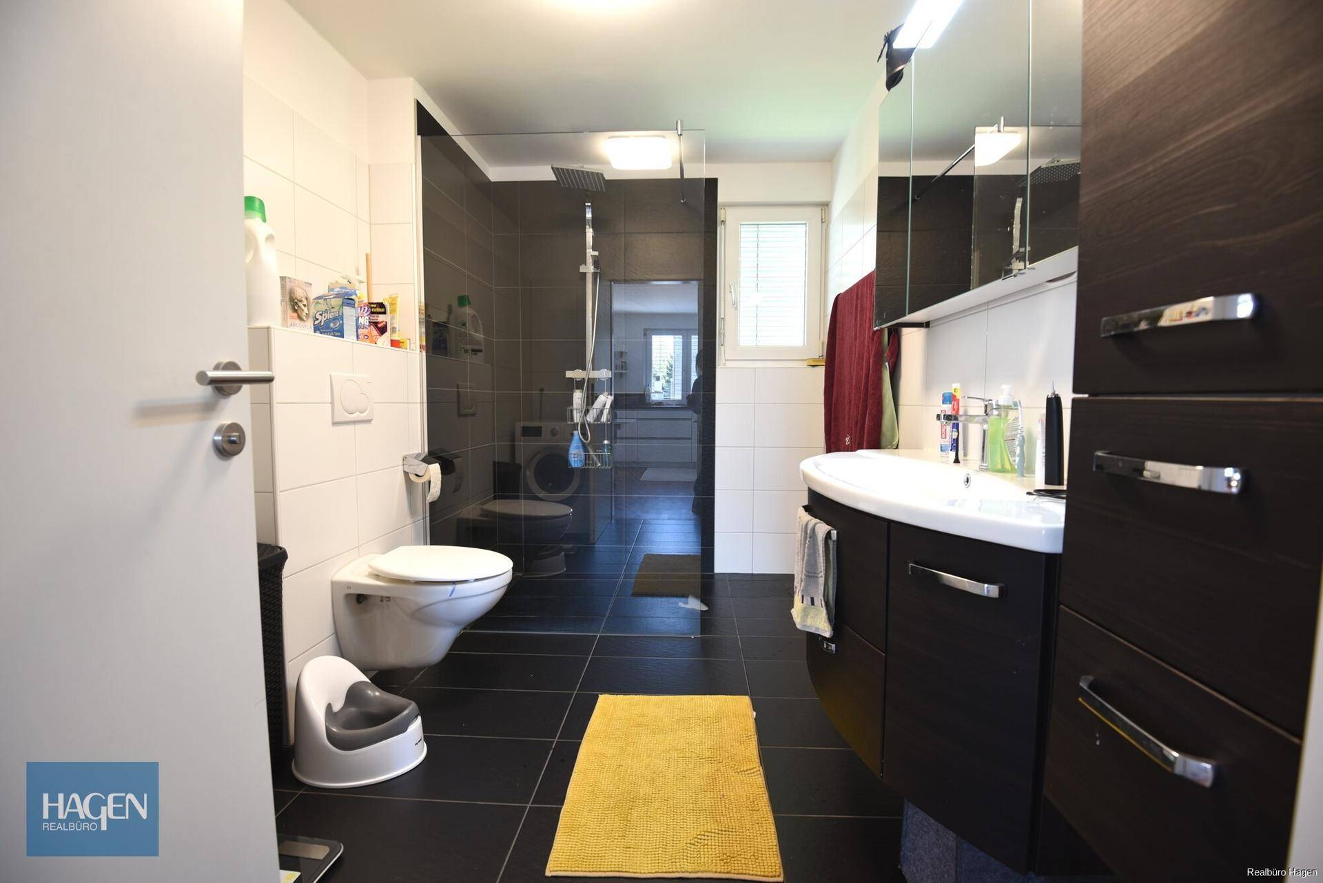 Modernes Badezimmer mit dunklen Fliesen, begehbarer Dusche, WC und Fenster.