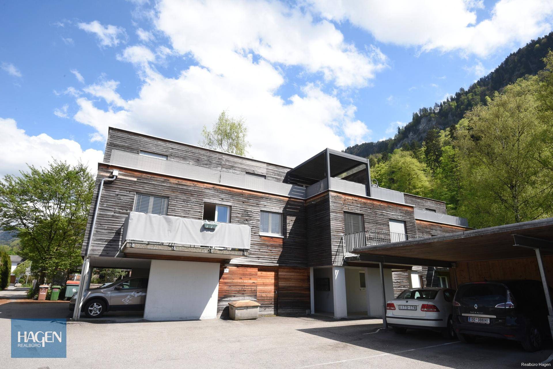Modernes Mehrfamilienhaus mit Holzfassade, Balkonen und Carports in grüner Umgebung.