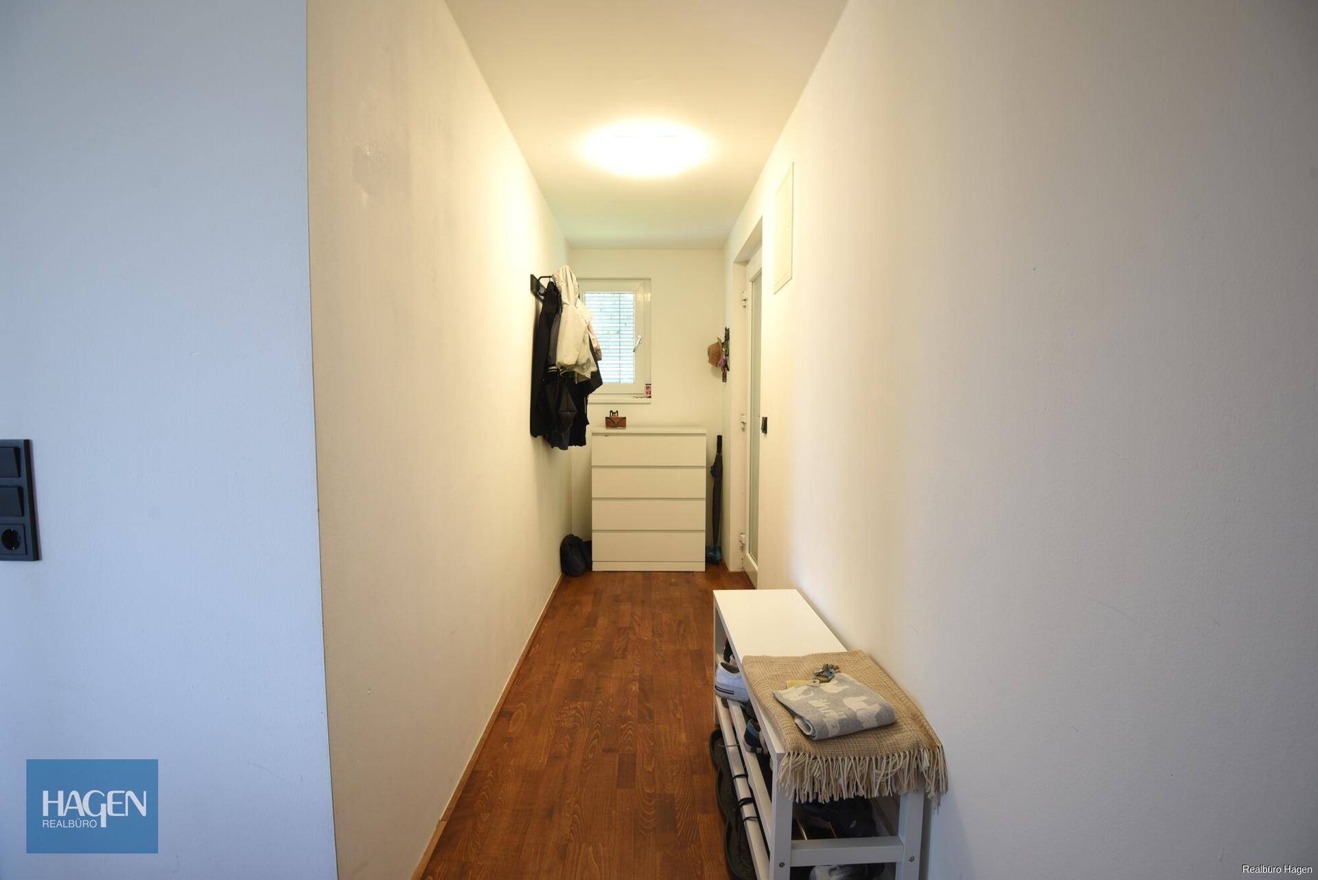 Heller Flur mit Holzboden, Garderobe und Kommode, der zu weiteren Räumen führt.