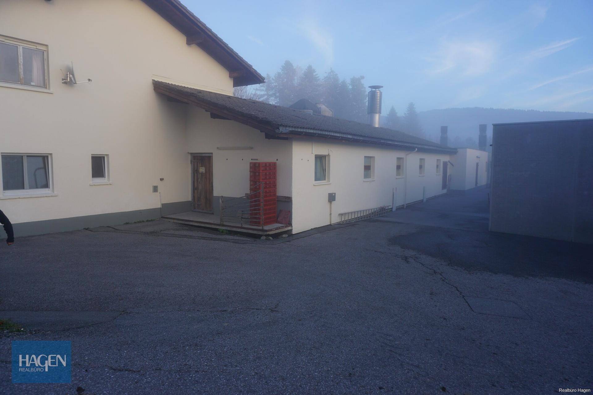 Seitenansicht eines Gebäudes mit Eingangsbereich und langer Fassade, umgeben von nebliger Morgenstimmung.