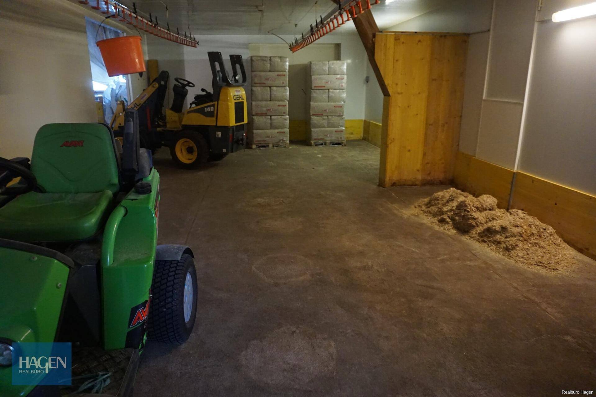 Lagerraum mit landwirtschaftlichen Maschinen, gestapelten Ballen und Holzspänen auf dem Boden.