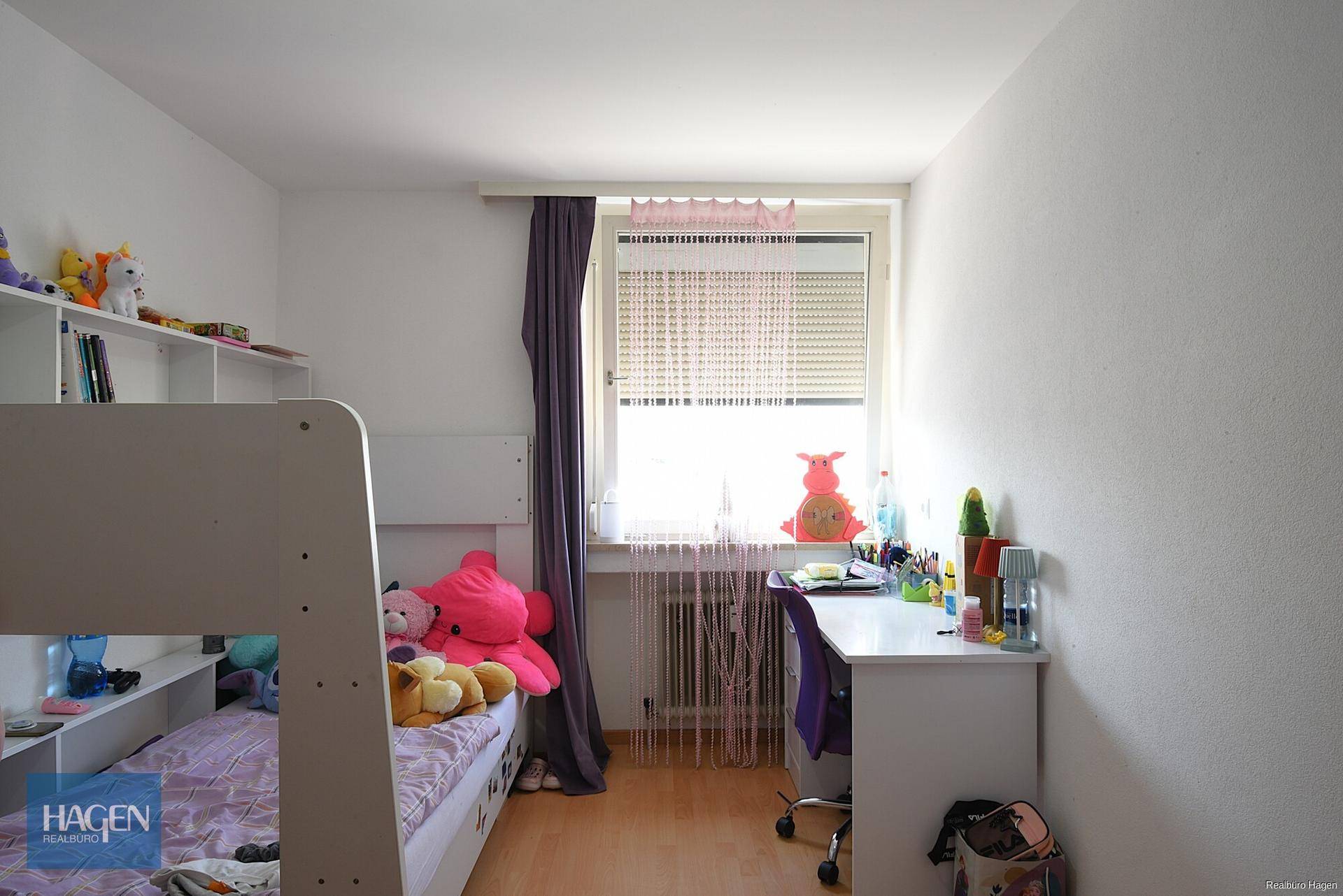 Helles Kinderzimmer mit Etagenbett, Schreibtisch und einem Fenster mit Jalousien.