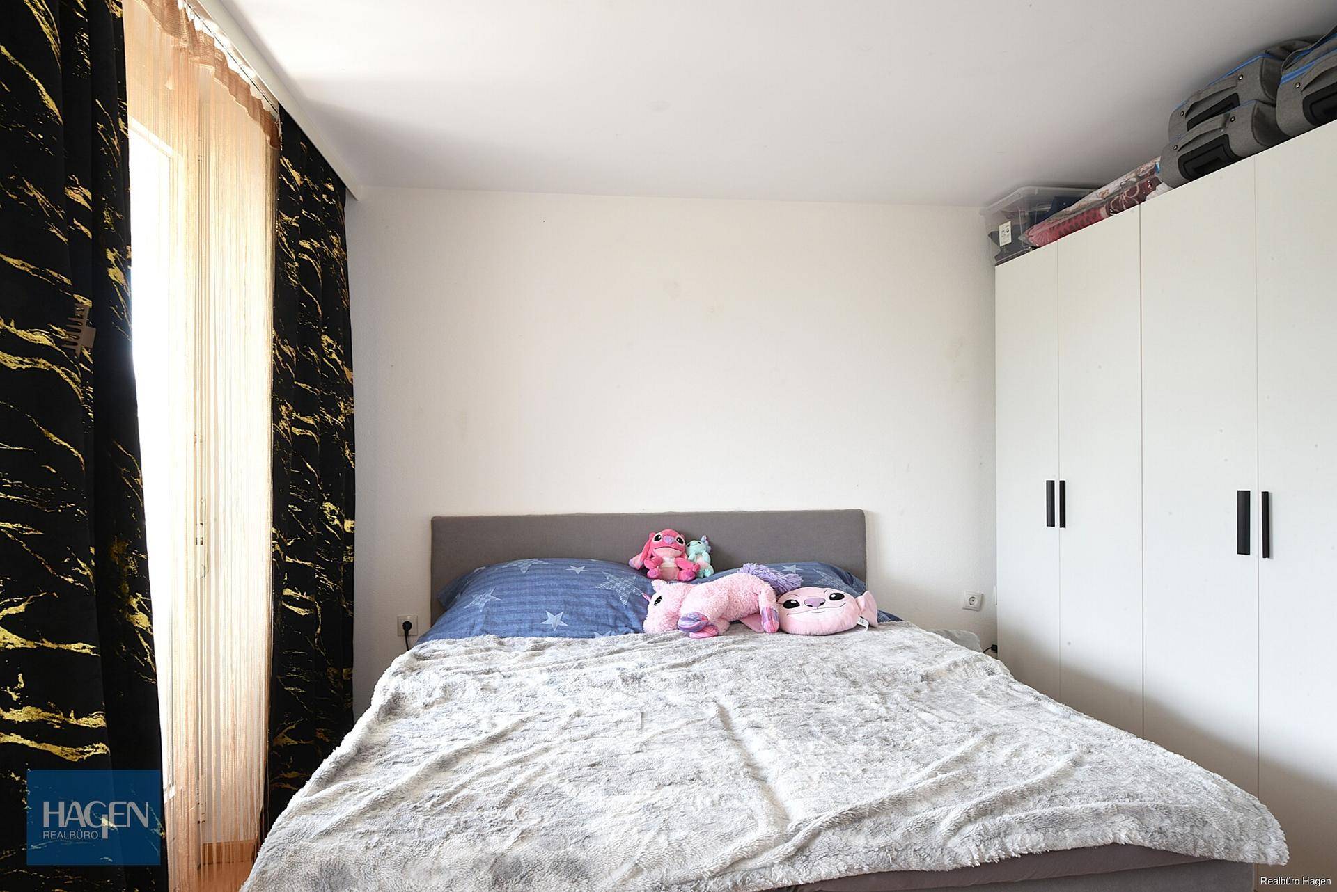 Schlafzimmer mit Doppelbett, weißem Kleiderschrank und dunklen Vorhängen.