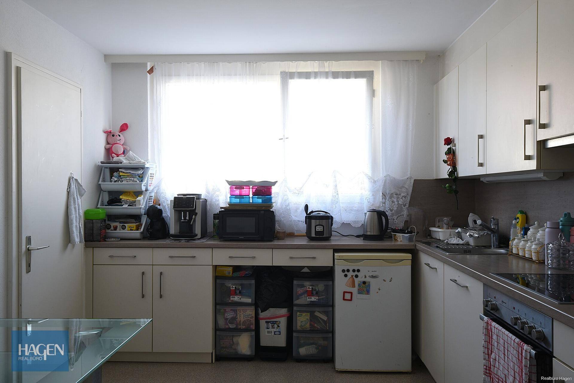 Funktionale Küche mit weißen Schränken, Arbeitsplatte und einem großen Fenster.