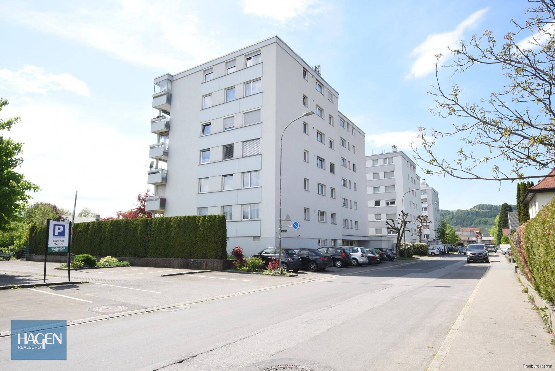 Mehrfamilienhaus mit mehreren Etagen, Balkonen und Parkplätzen im Freien.