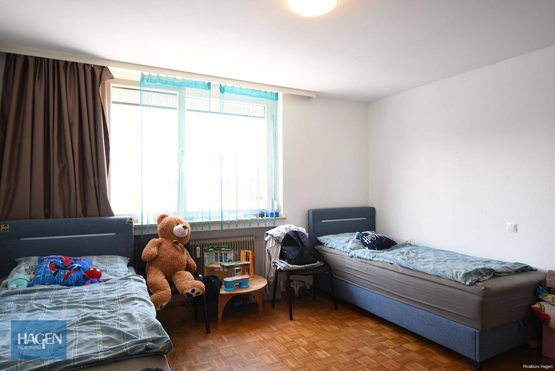 Kinderzimmer mit zwei Einzelbetten, Holzboden und einem großen Fenster für viel Licht.