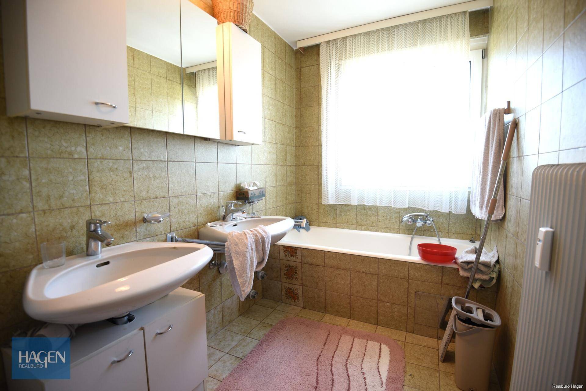 Badezimmer im 80er-Jahre-Stil mit Badewanne, Doppelwaschbecken und Fenster.