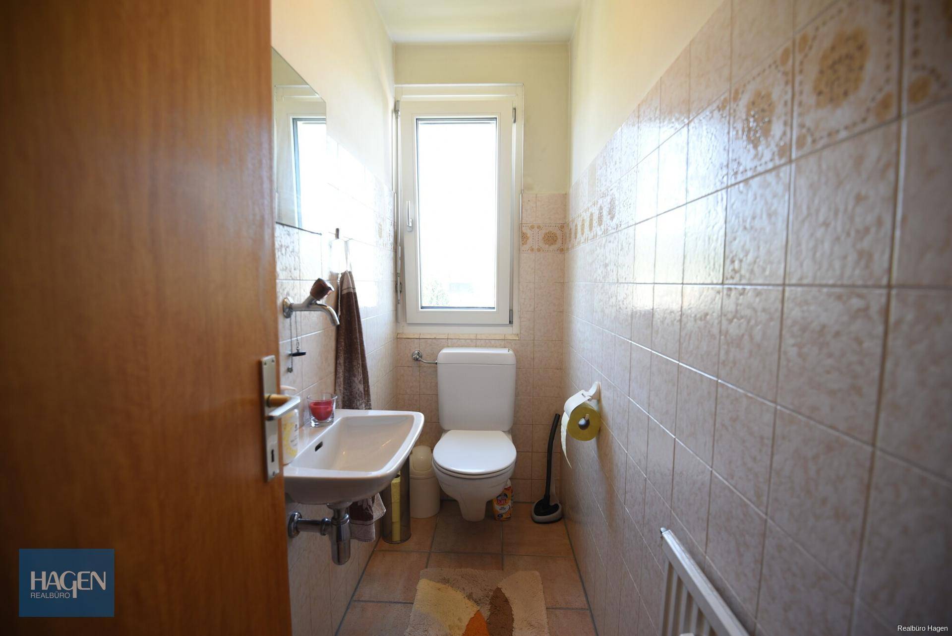 Separates WC mit Waschbecken, Toilette, Fenster und Fliesen an den Wänden.