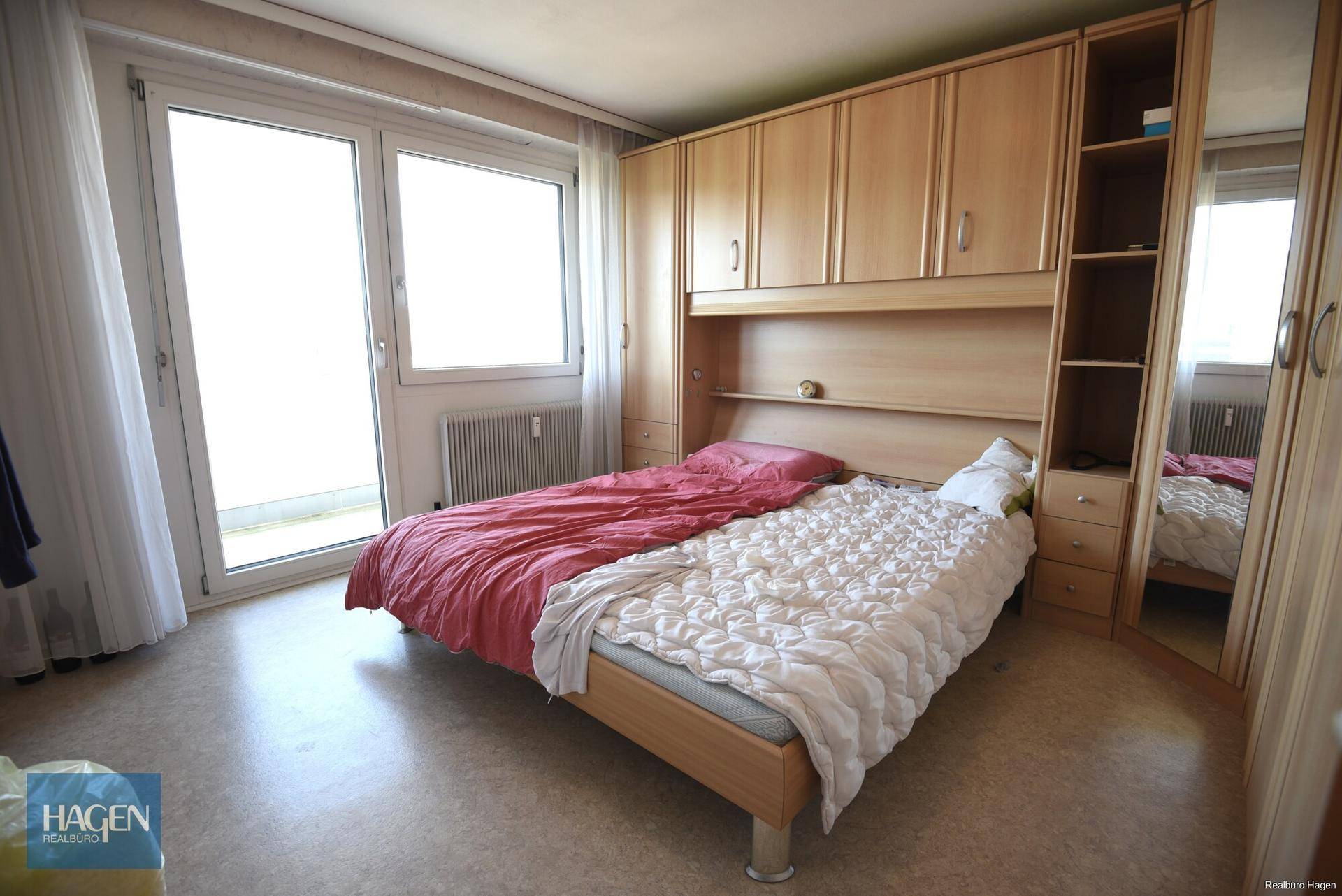 Schlafzimmer mit Einbauschränken, Doppelbett, Vinylboden und Balkonzugang.