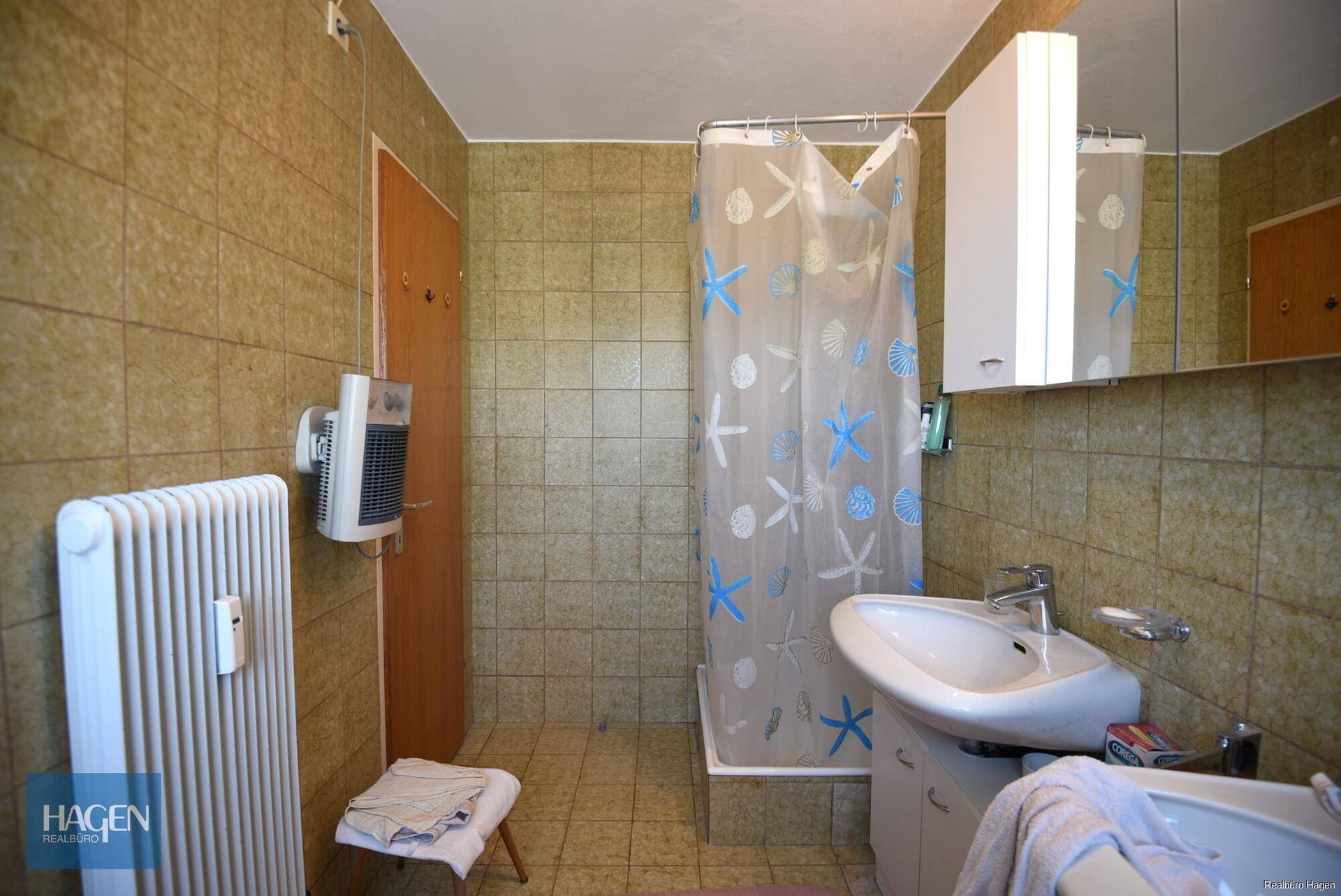 Badezimmer im 80er-Jahre-Stil mit Dusche, Waschbecken und Fliesen an den Wänden.