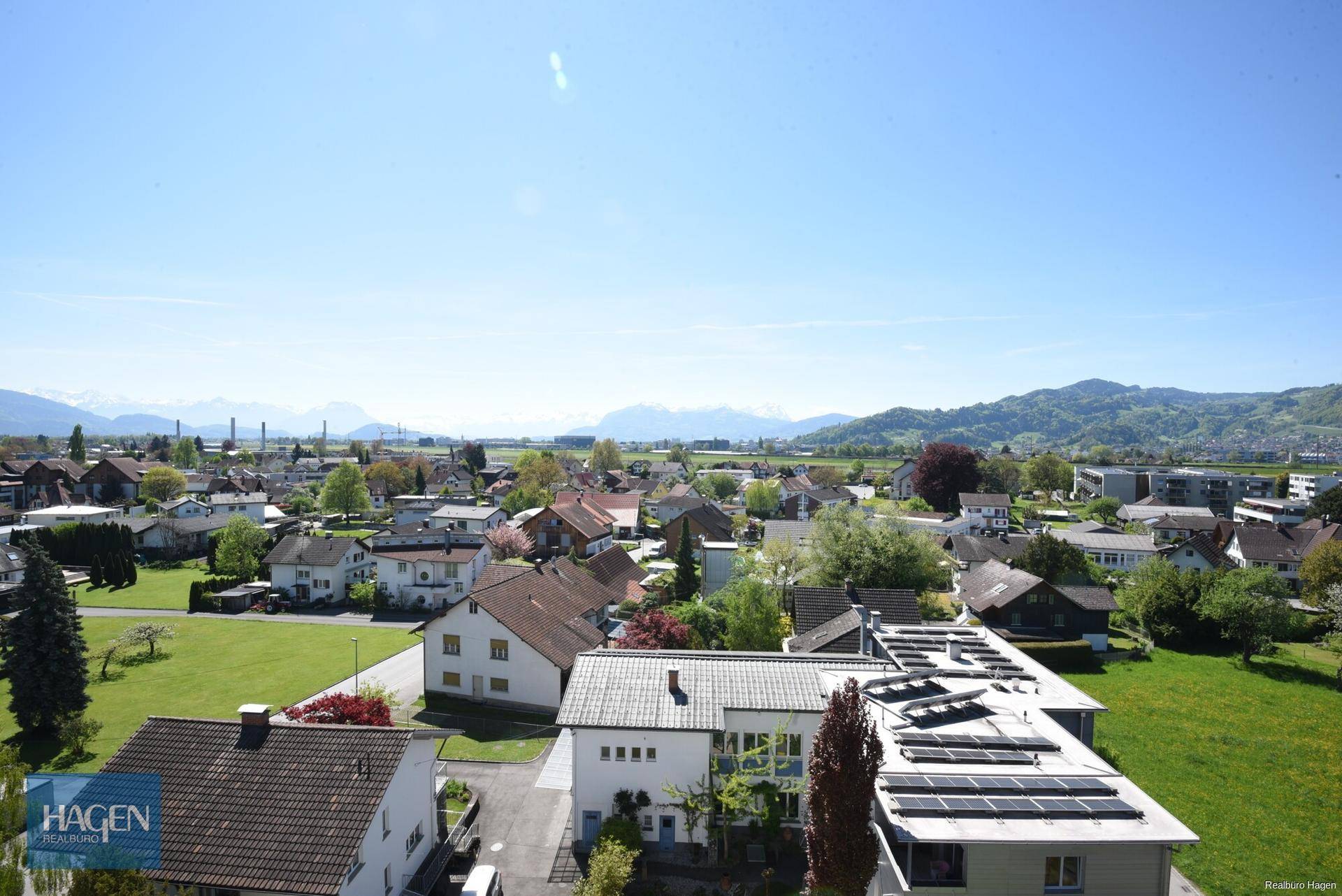 Weitläufiger Blick über die umliegende Landschaft, Häuser und Berge unter blauem Himmel.