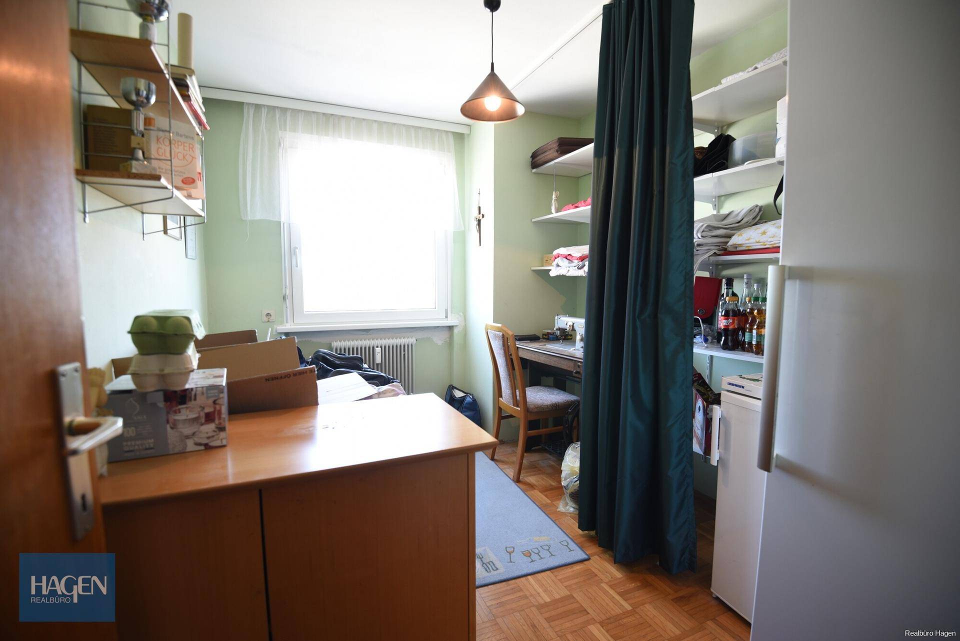 Kleines Zimmer mit Schreibtisch, Regal, Fenster und Parkettboden.