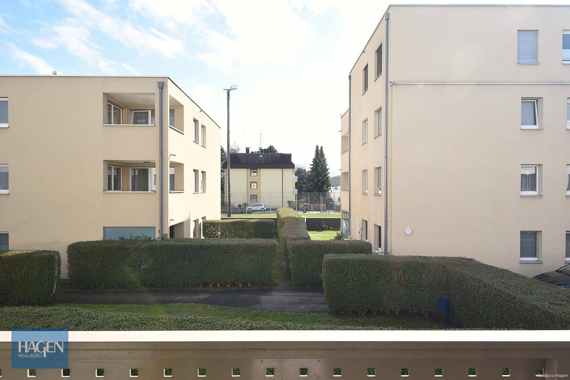 Blick von einem Balkon auf die gepflegten Grünflächen und die umliegenden Wohngebäude.
