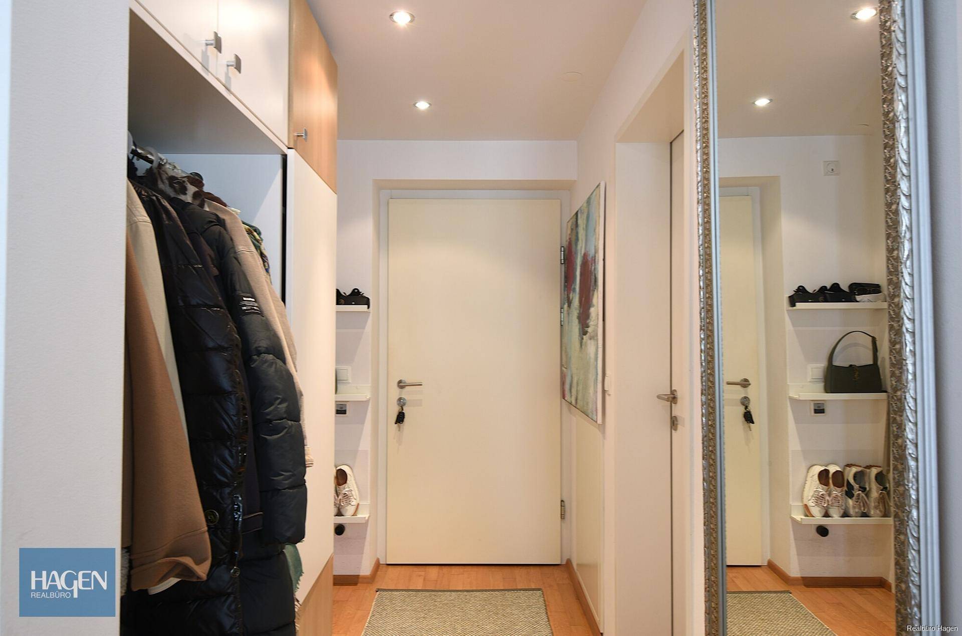 Heller Eingangsbereich mit Garderobe, Schuhablagen und einem großen Wandspiegel.