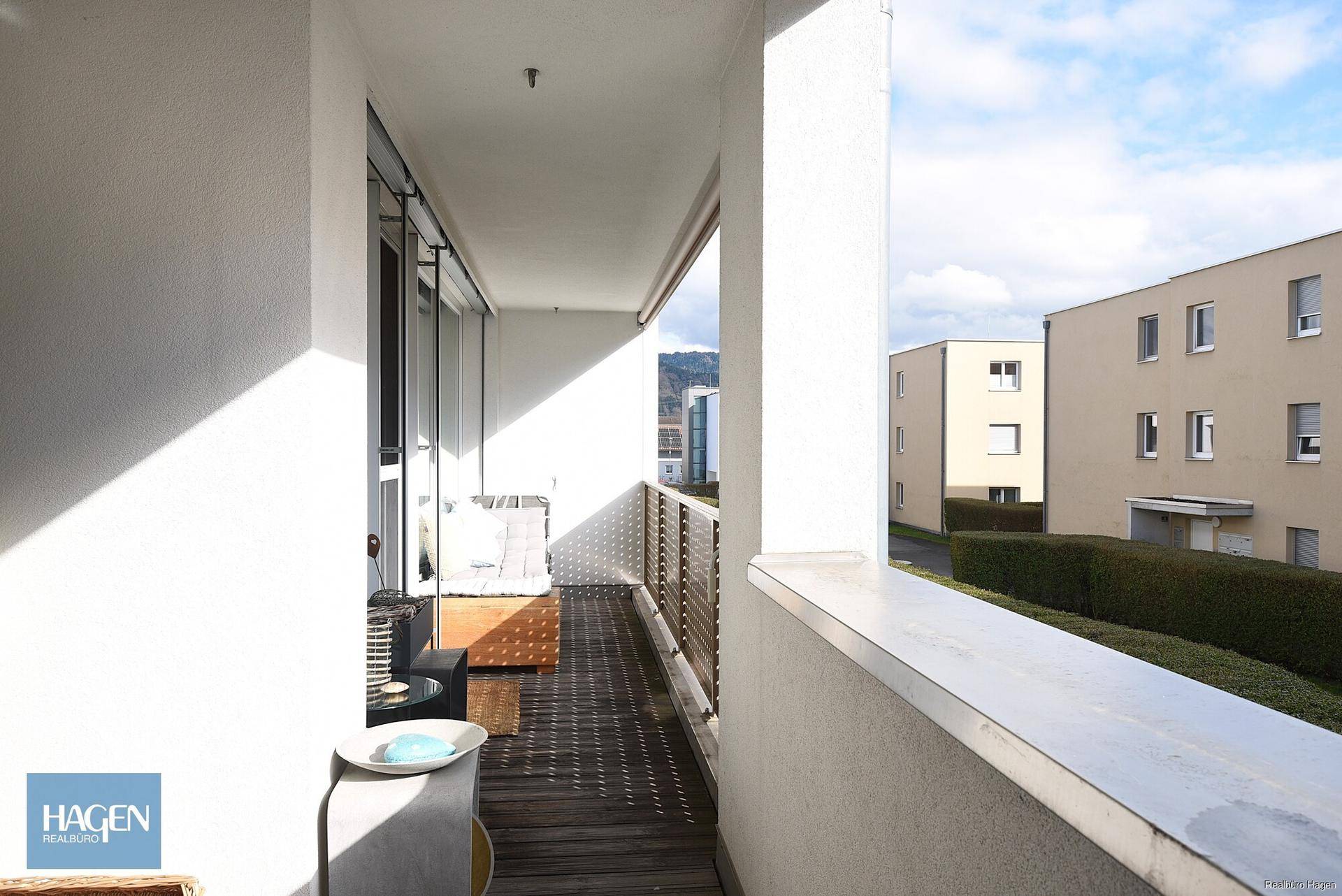 Geräumiger Balkon mit Holzboden und Blick auf die umliegenden Wohngebäude und Grünflächen.