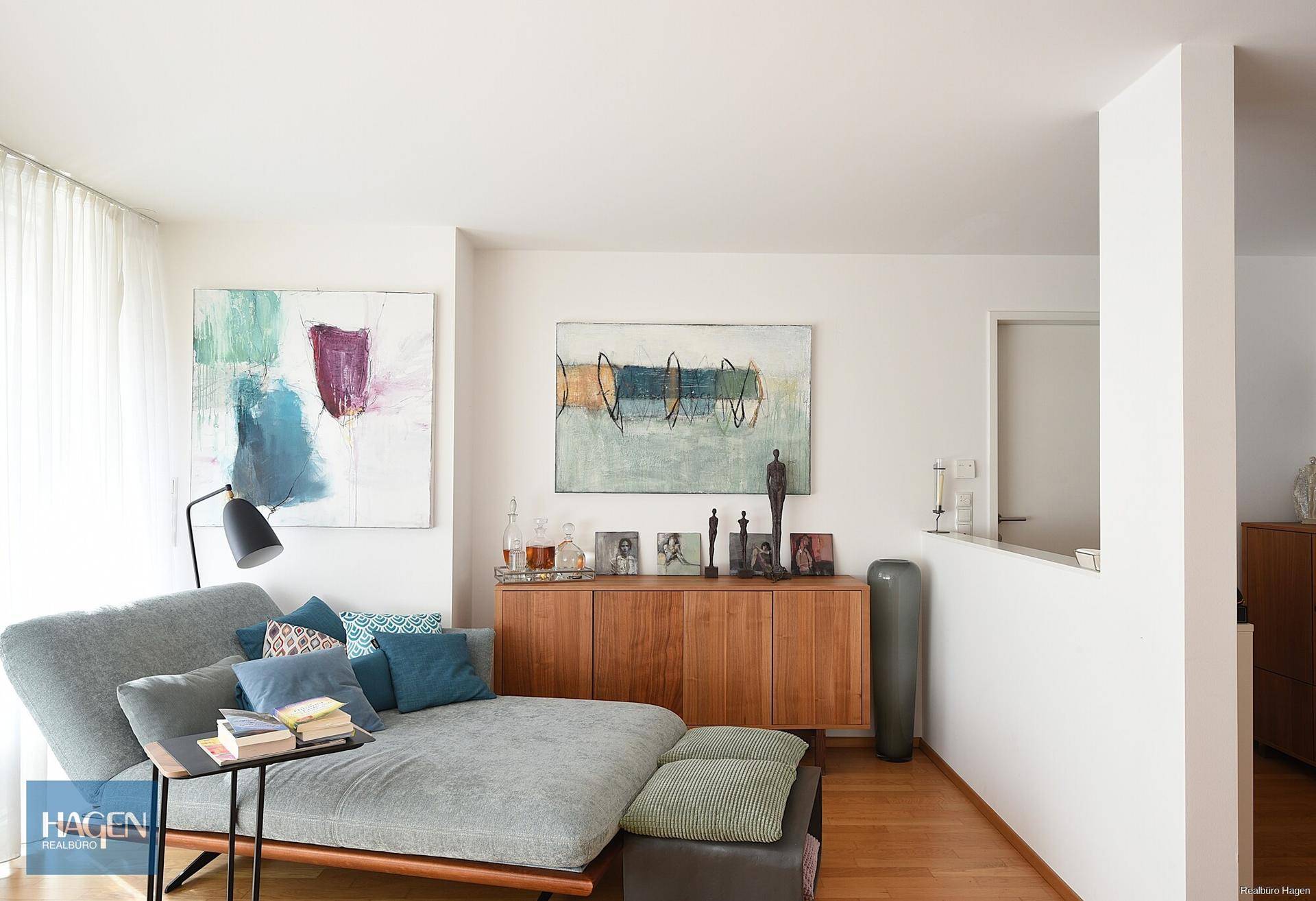 Gemütliches Wohnzimmer mit moderner Einrichtung, Holzboden und farbenfrohen Kunstwerken.