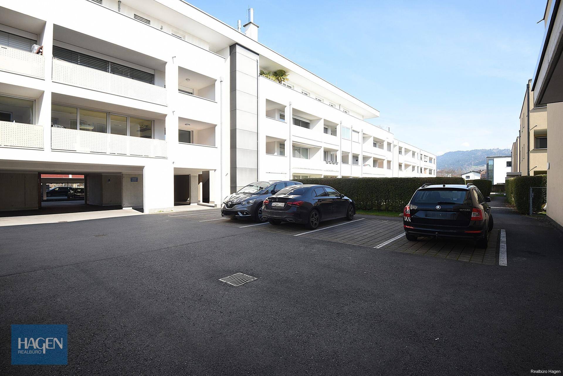 Außenansicht eines modernen Wohnkomplexes mit Parkplätzen und gepflegten Hecken.