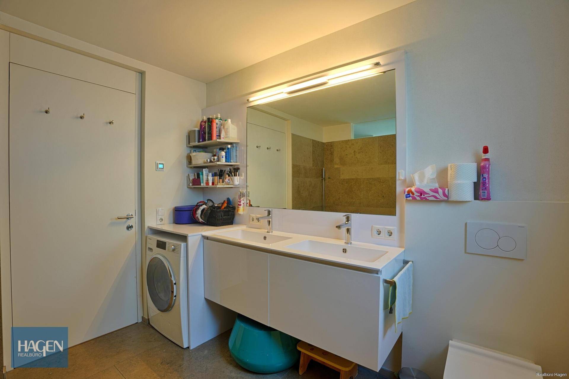 Geräumiges Badezimmer mit Doppelwaschbecken, großem Spiegel und integrierter Waschmaschine.