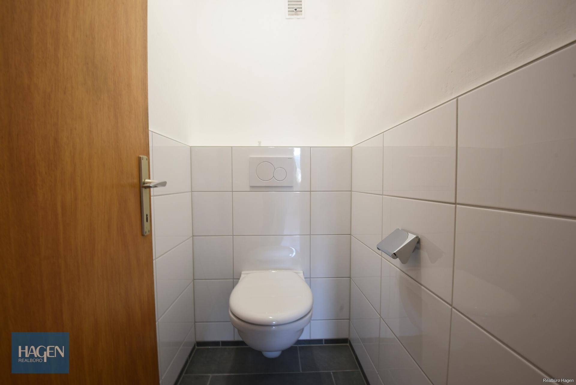 Separates WC mit wandhängender Toilette und weißen Fliesen, funktional und sauber.