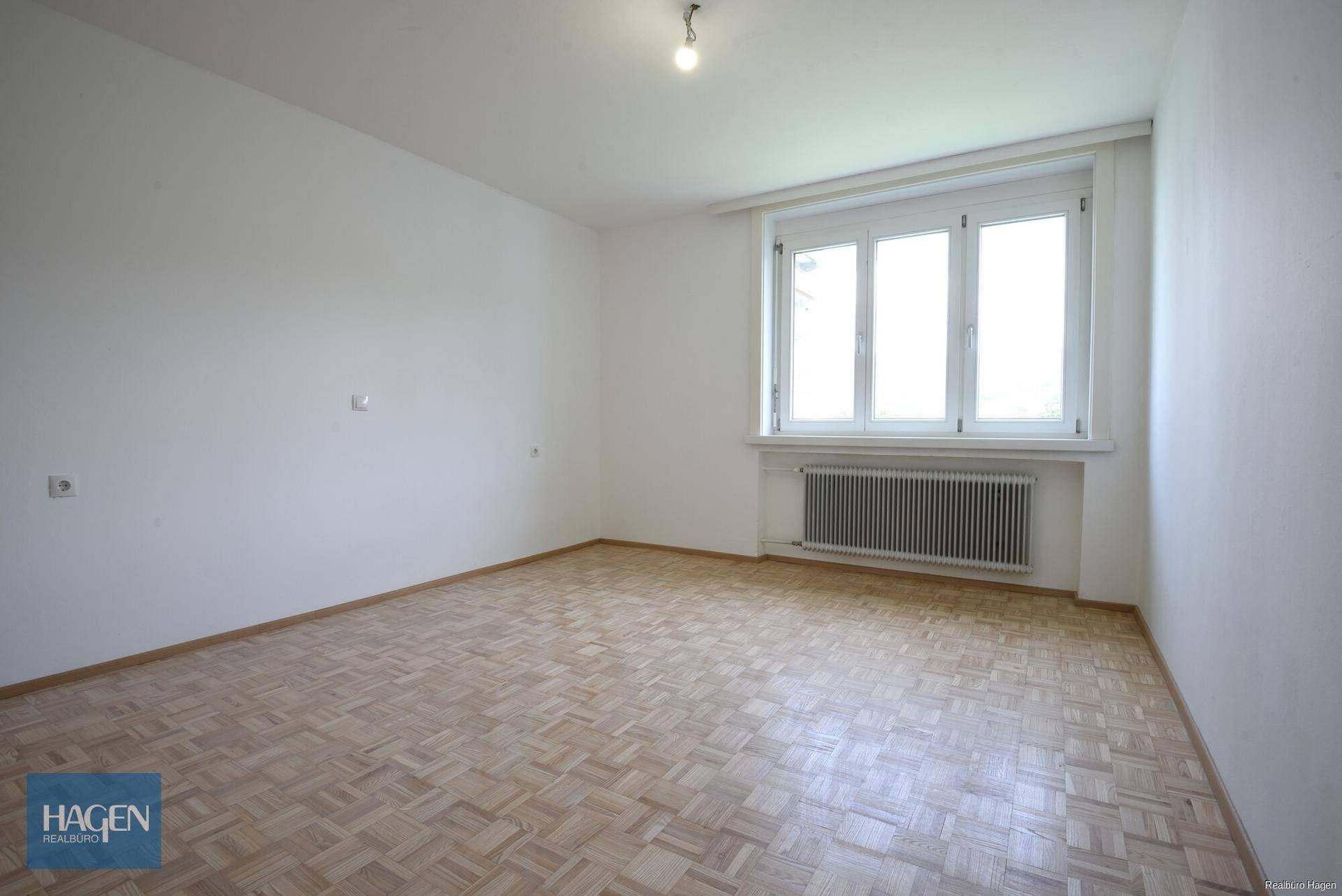Geräumiges, helles Zimmer mit Parkettboden und Fenster, ideal für Wohn- oder Schlafbereich.