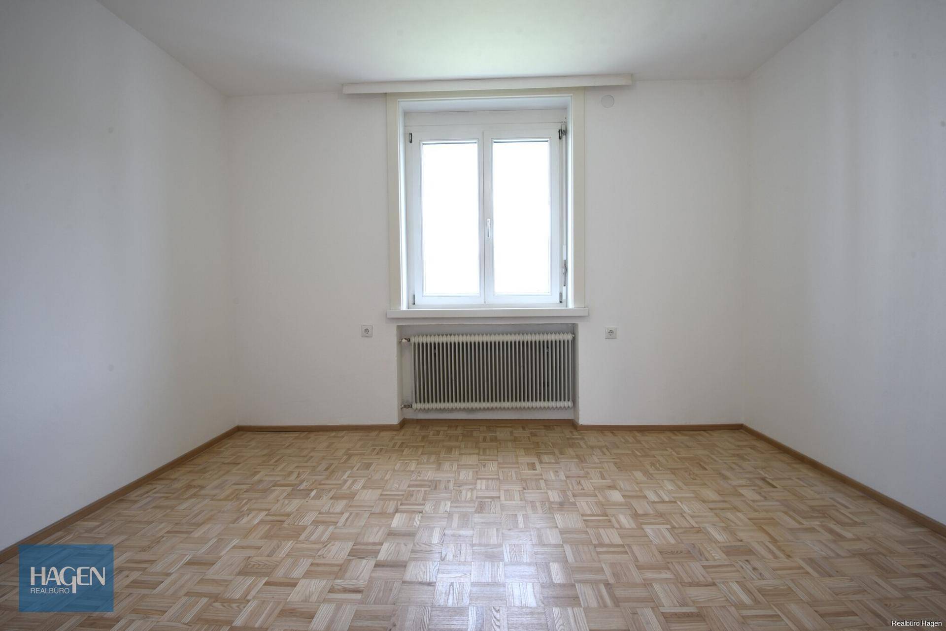 Helles, leeres Zimmer mit Parkettboden und großem Fenster, bereit zur individuellen Gestaltung.
