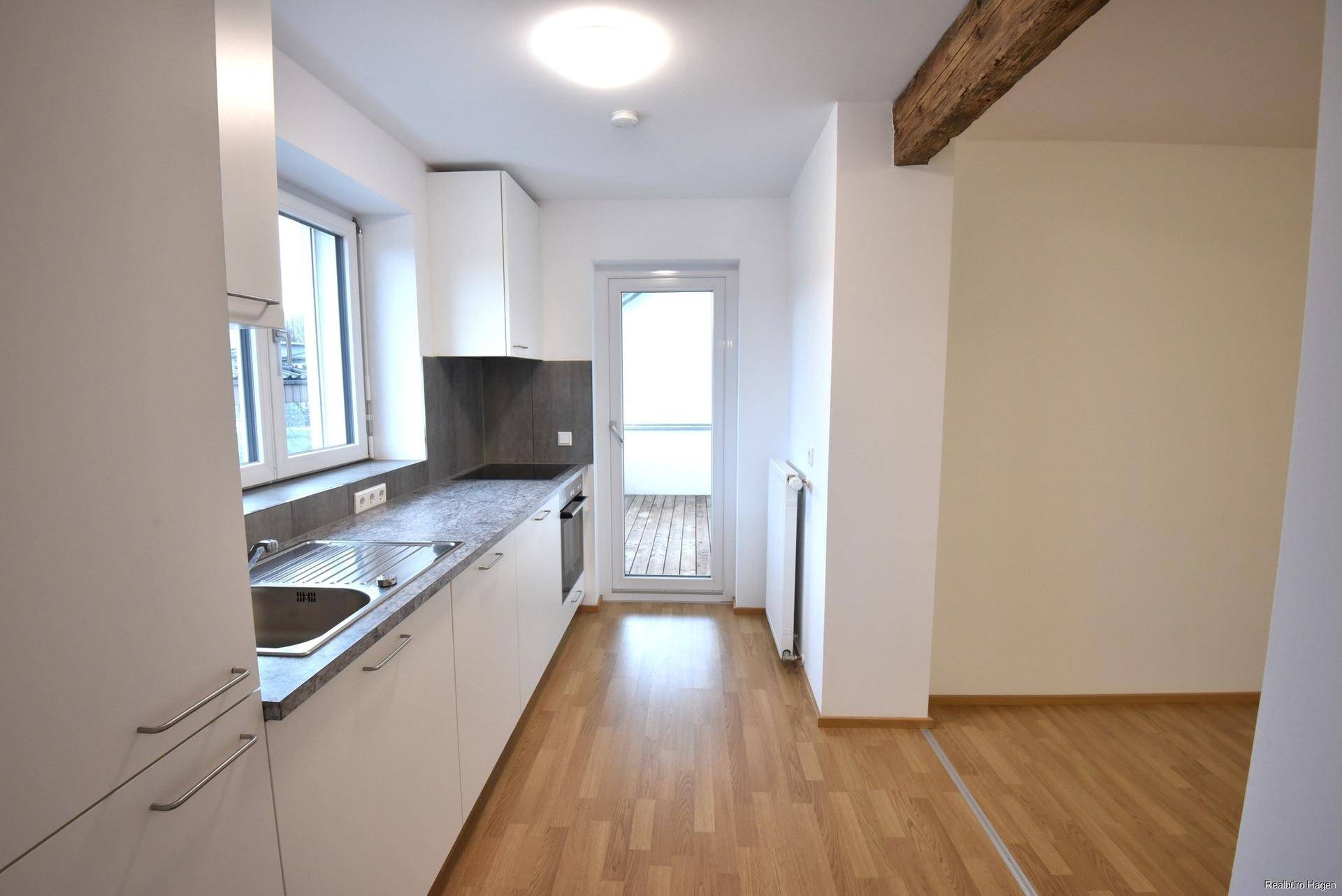 Moderne Einbauküche mit weißen Schränken, dunkler Arbeitsplatte und Zugang zum Balkon.