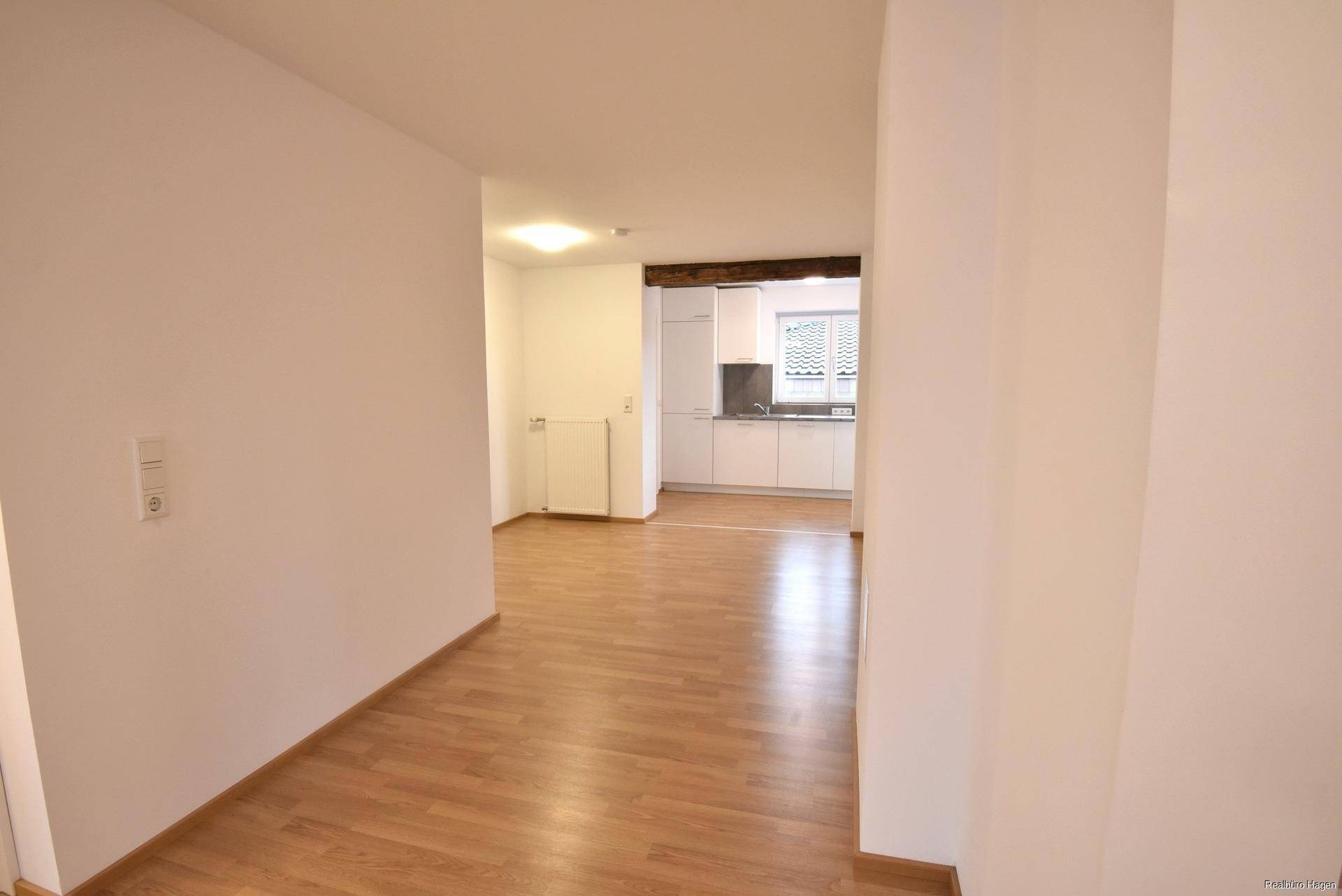 Offener Wohnbereich mit Laminatboden und Blick auf die angrenzende, helle Küche.