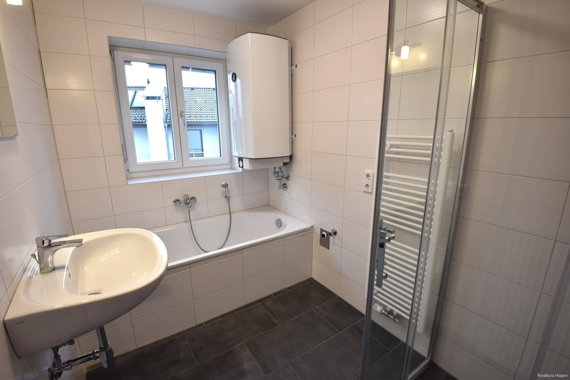Modern gefliestes Badezimmer mit Badewanne, Duschkabine und beheiztem Handtuchhalter.