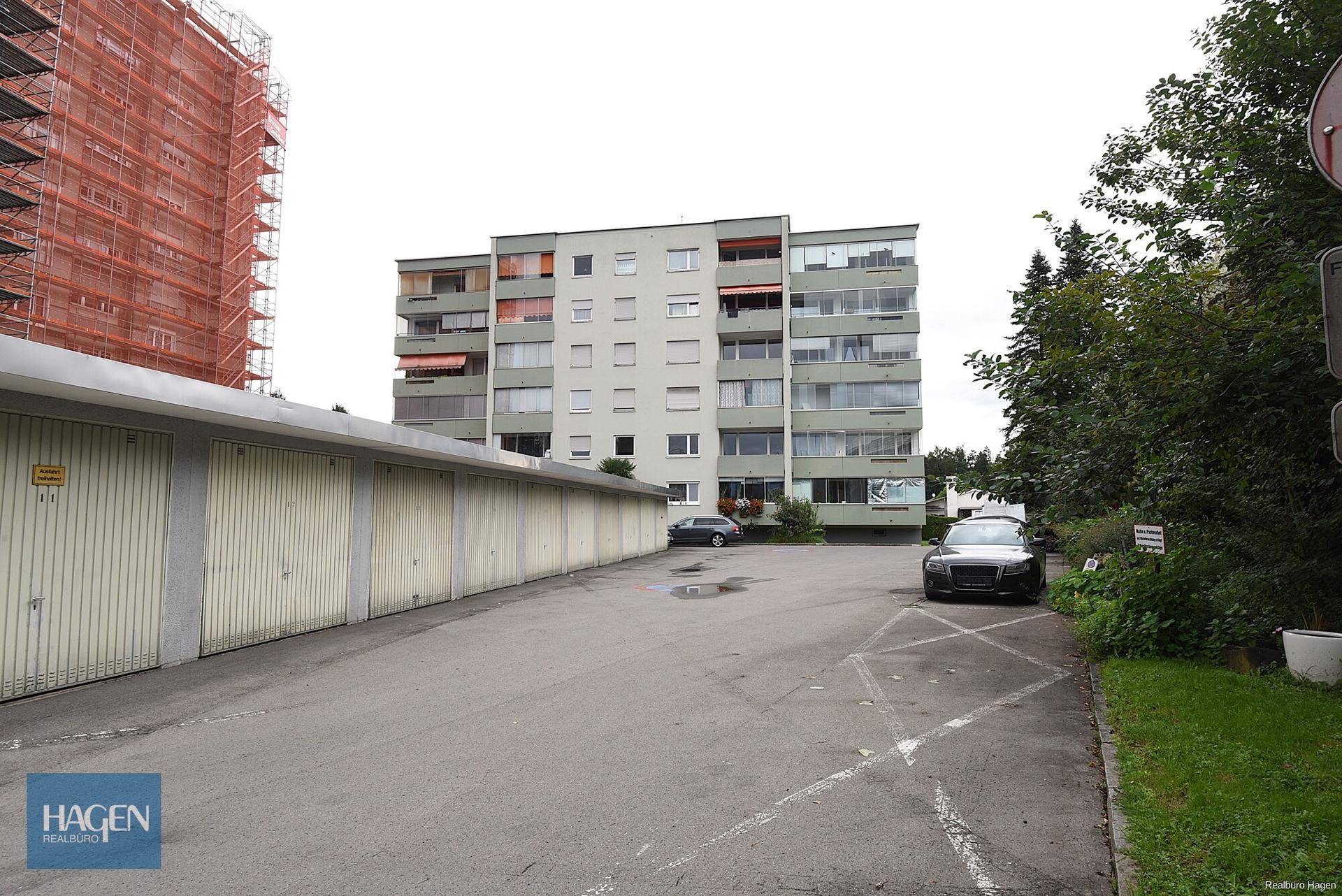 Mehrfamilienhaus mit Garagen und Parkplätzen in städtischer Umgebung.