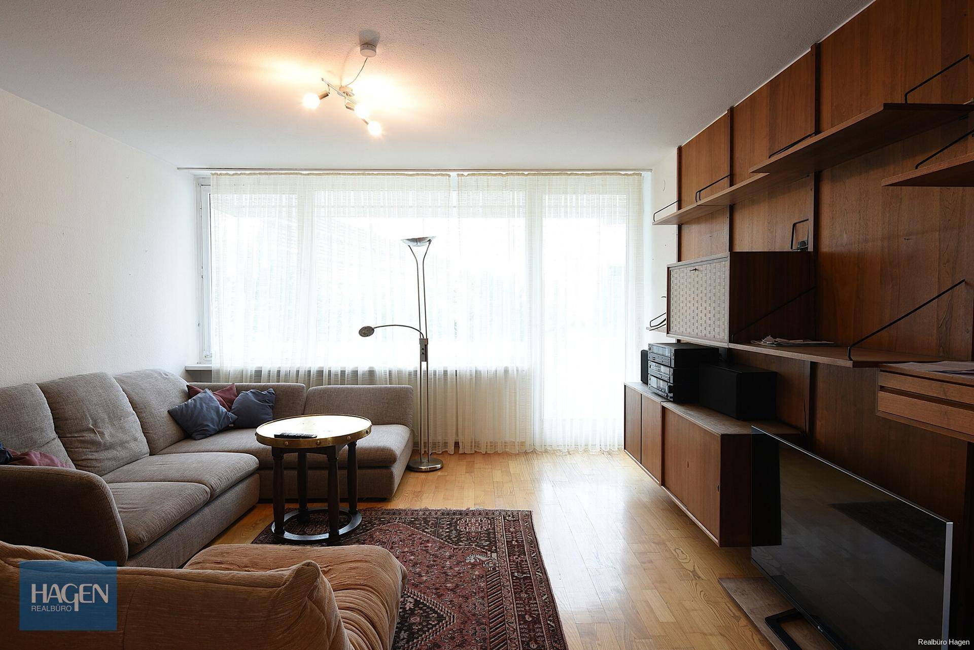 Helles Wohnzimmer mit großem Sofa, Holzwandregal und Parkettboden.