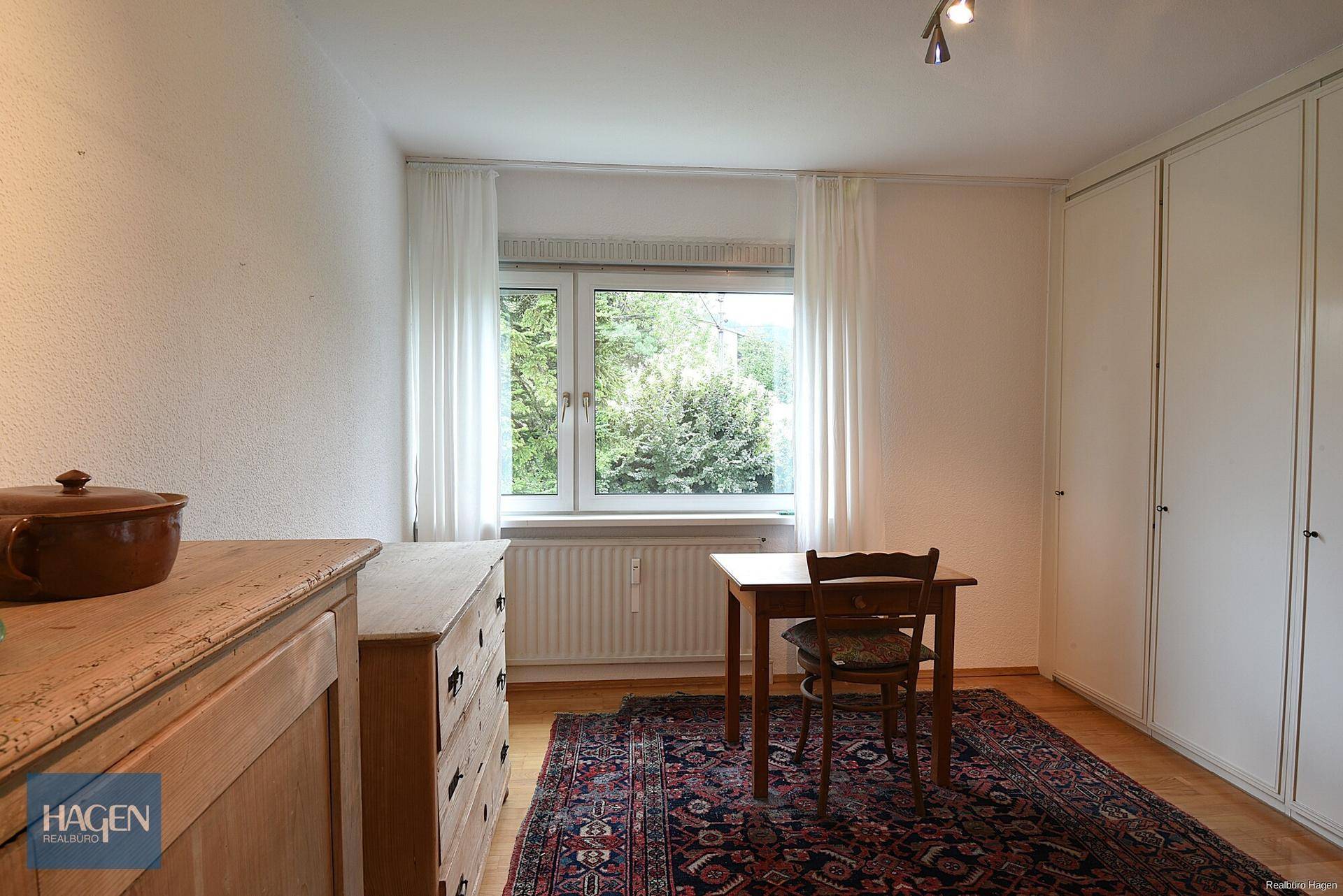 Schlafzimmer mit Holzboden, Schreibtisch und Einbauschränken, Blick ins Grüne.