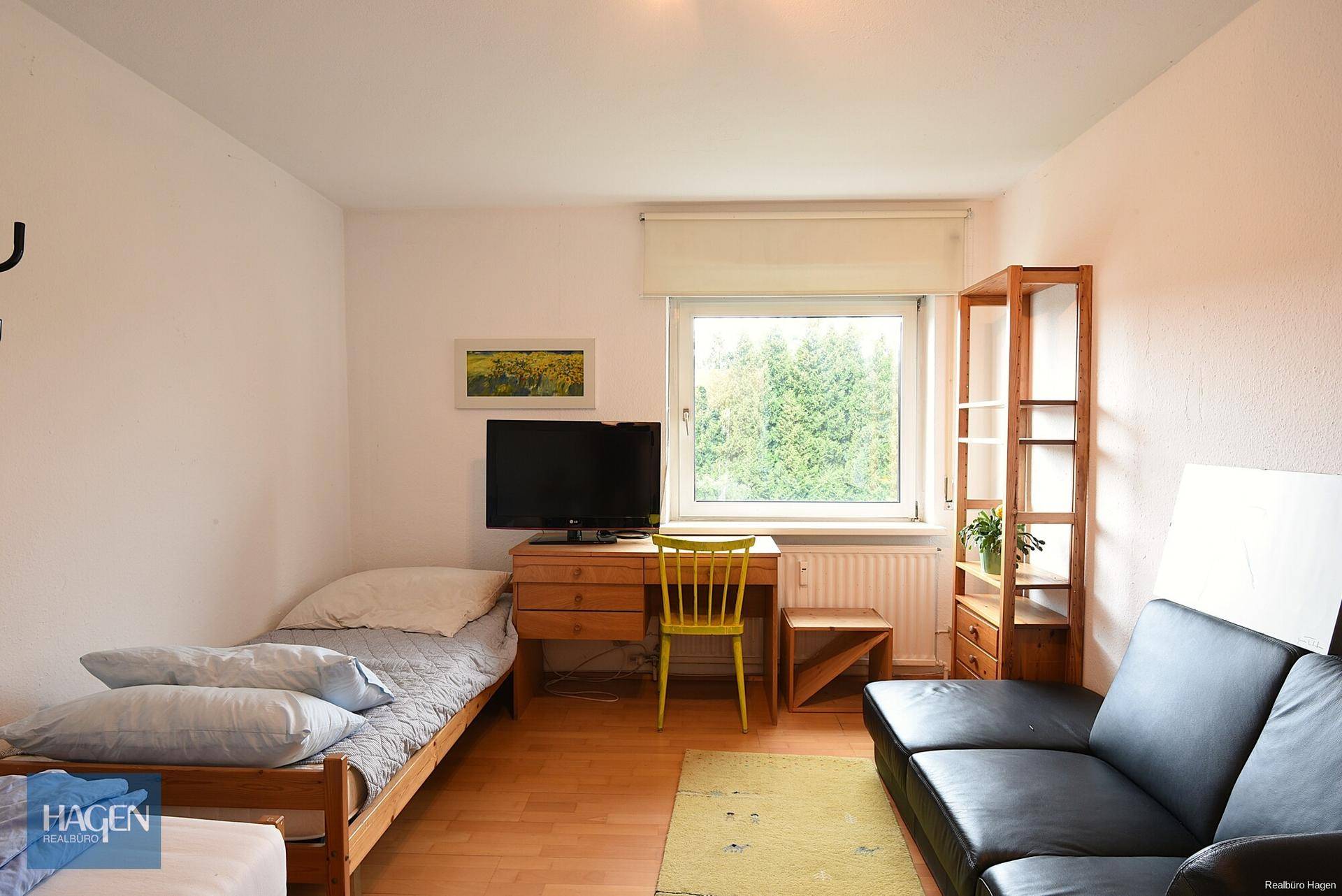 Helles Schlafzimmer mit Einzelbett, Sofa und Holzboden, Blick ins Grüne.