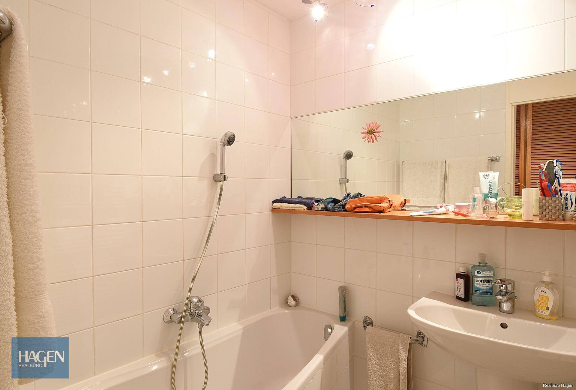 Helles Badezimmer mit weißen Fliesen, Badewanne und Einzelwaschbecken.