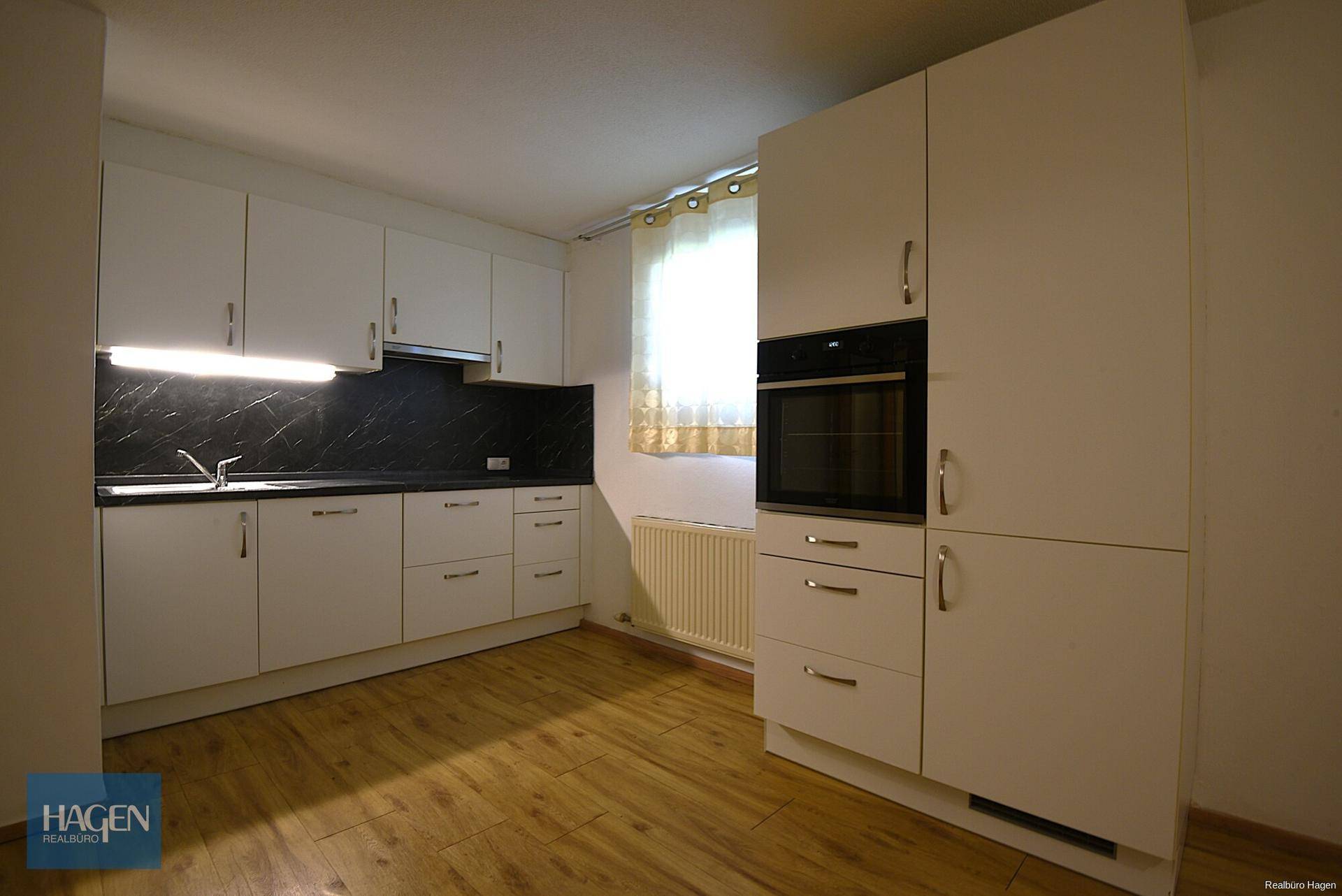 Helle Küche mit weißen Schränken, dunkler Arbeitsplatte und integriertem Backofen.