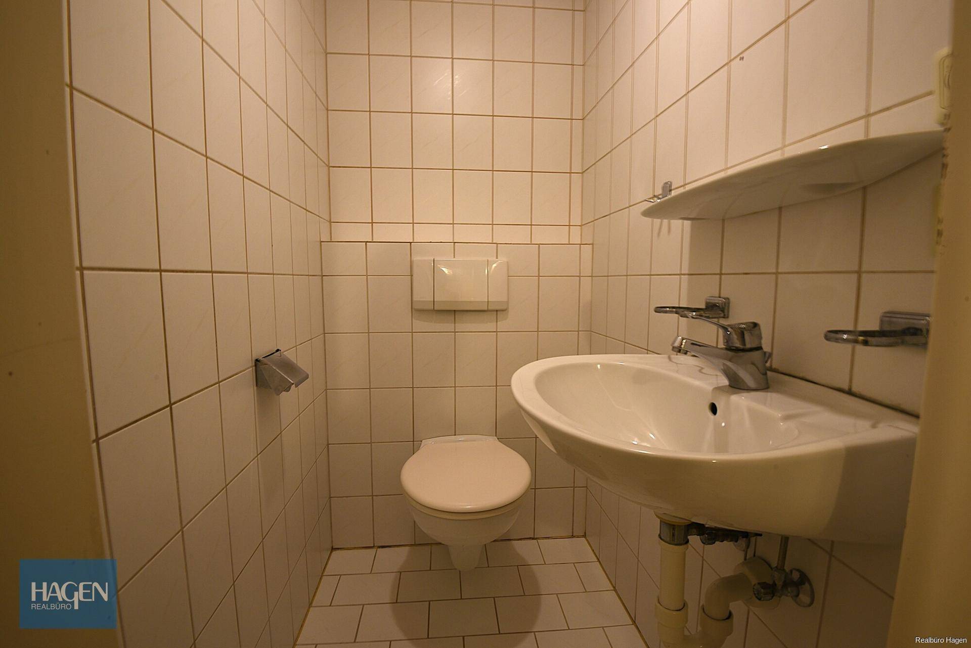 Kleines Gäste-WC mit weißen Fliesen, wandhängendem WC und Waschbecken.