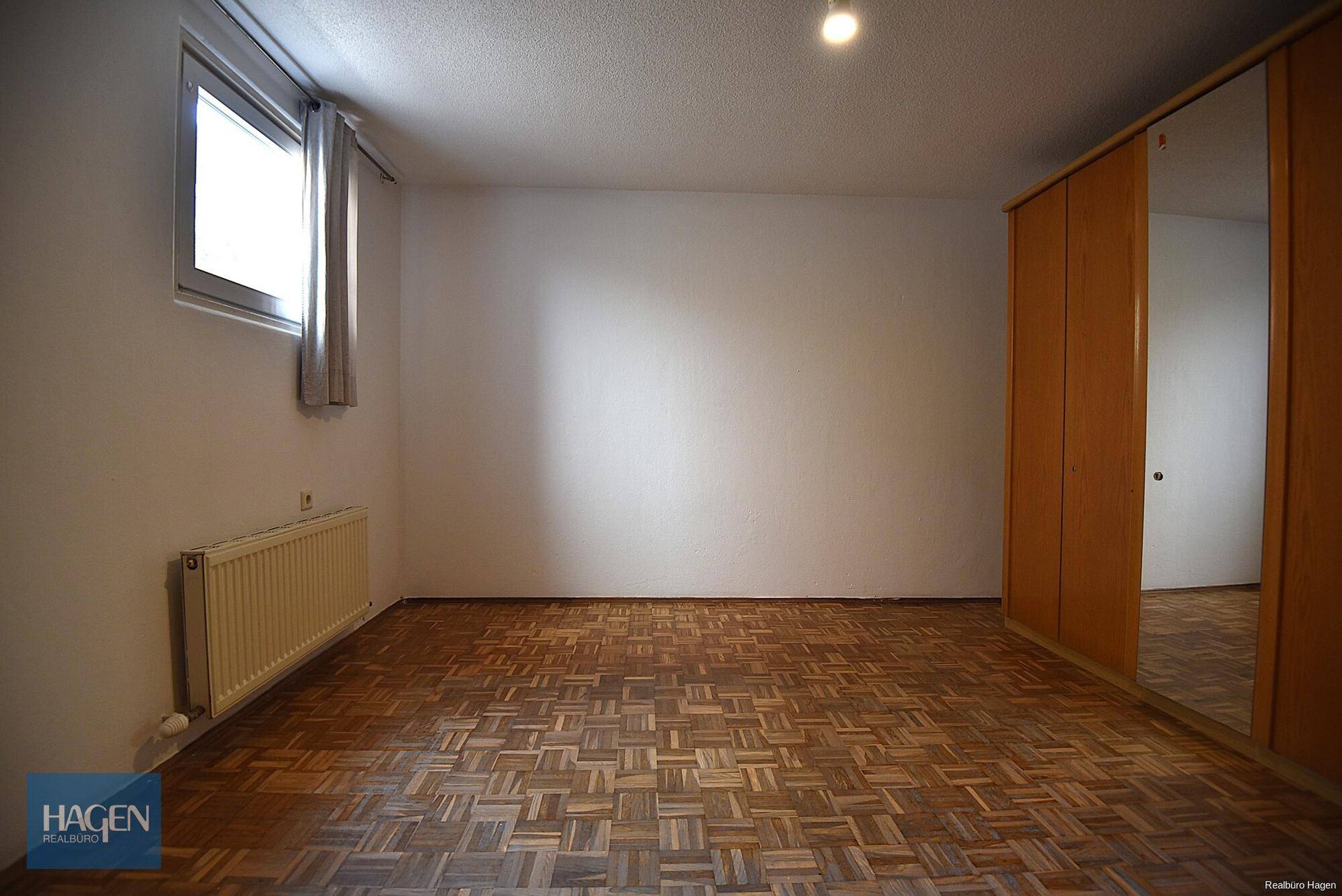 Schlafzimmer mit Parkettboden, großem Fenster und Spiegelschrank.