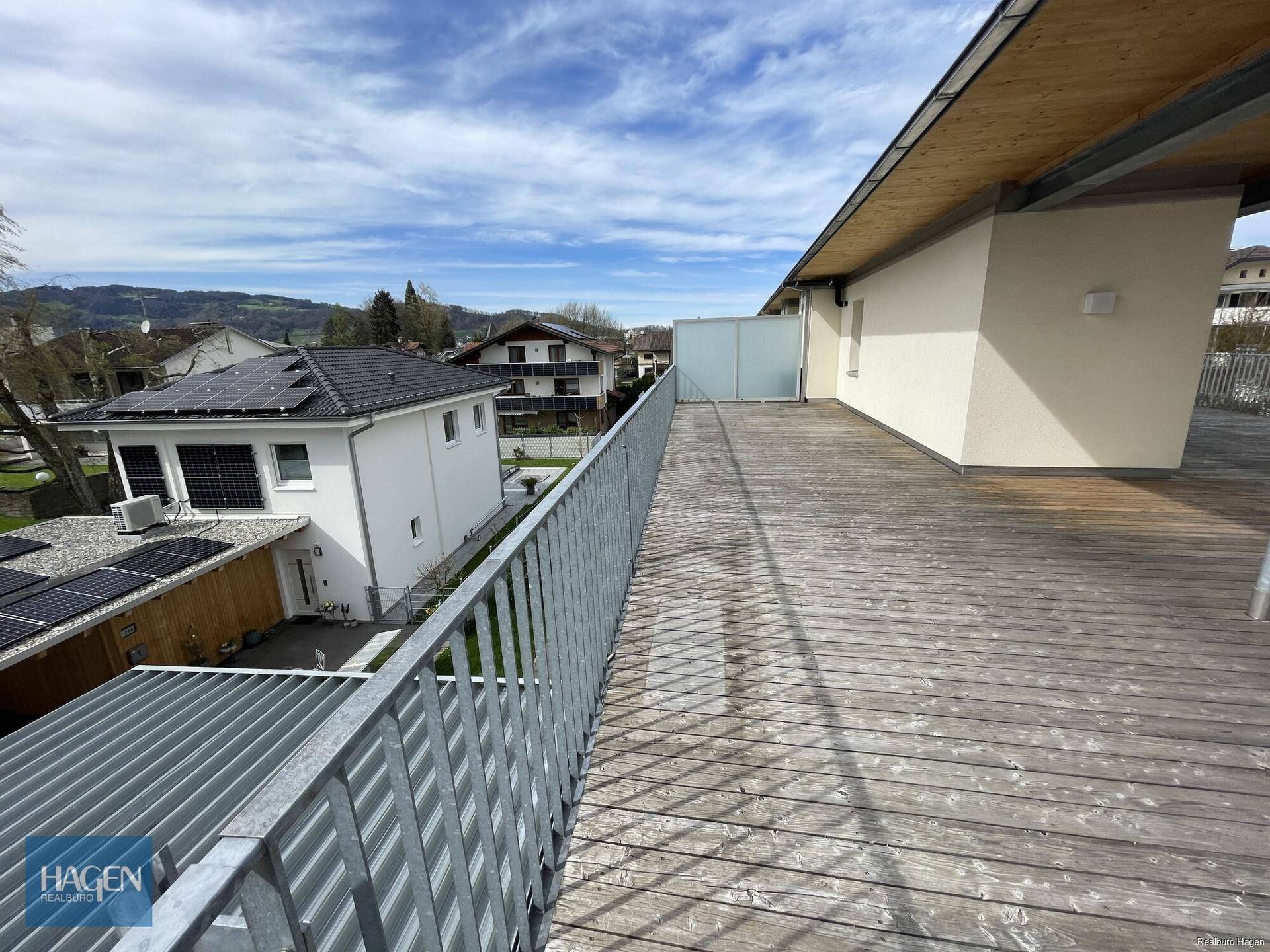 Weitläufige Holzterrasse mit Metallgeländer und Blick auf die umliegende Landschaft und Berge.