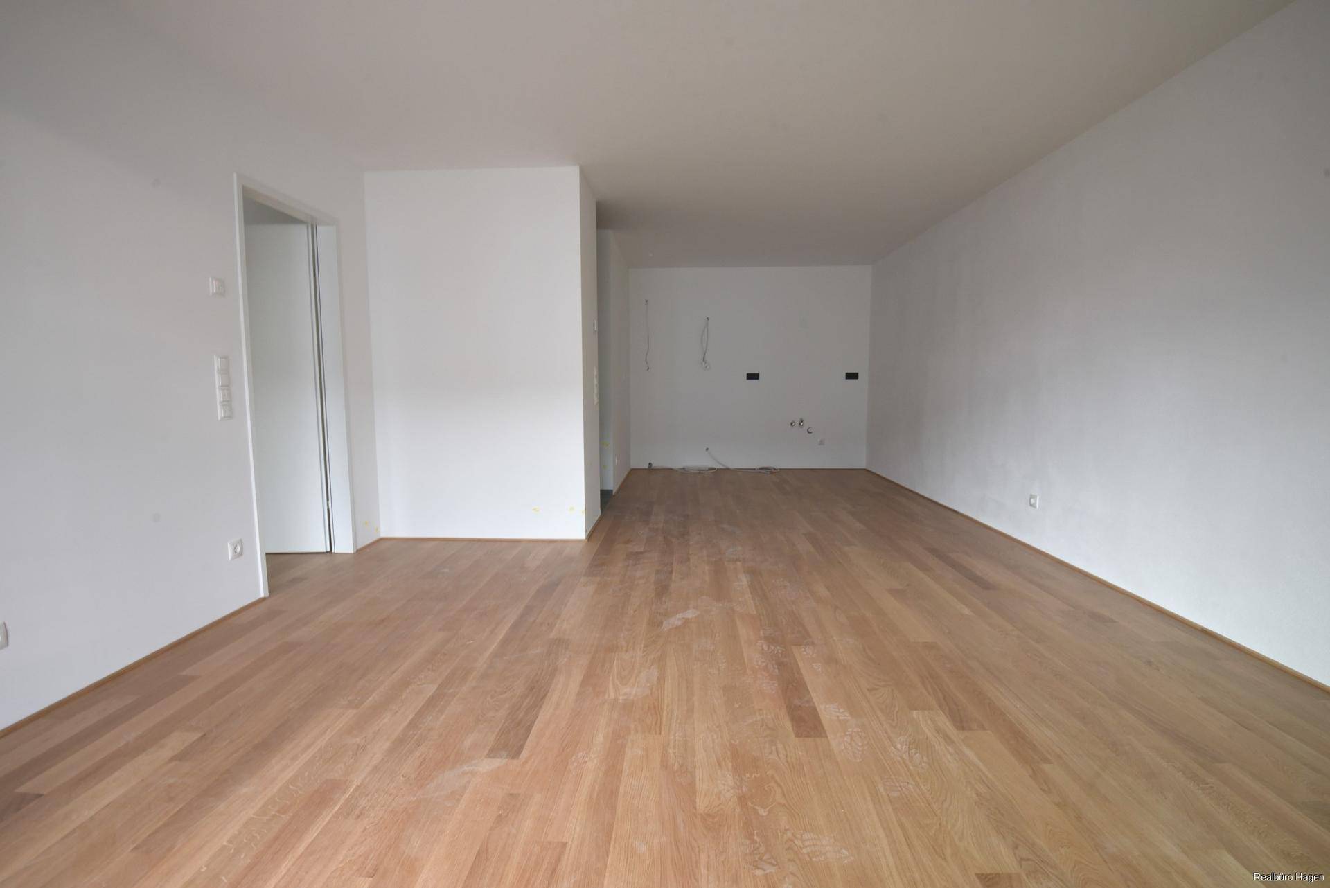 Geräumiger, heller Wohnbereich mit neuem Parkettboden und weißen Wänden.